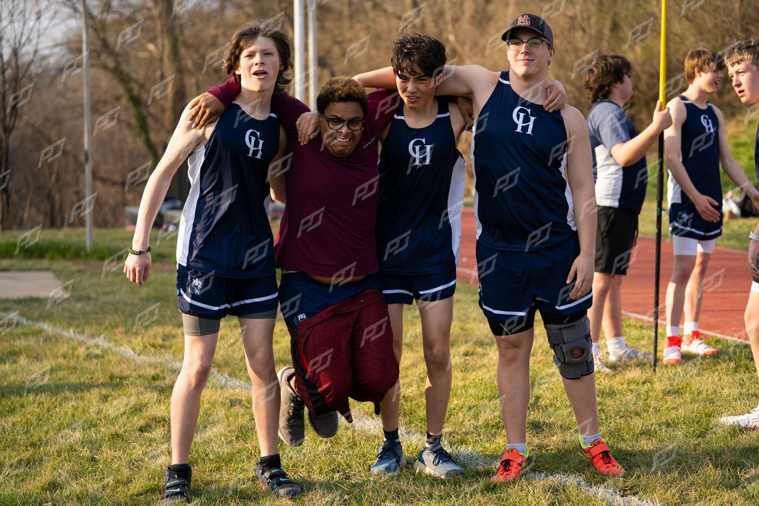 Three high school track athletes in blue CH uniforms support a teammate at an outdoor track and field meet.