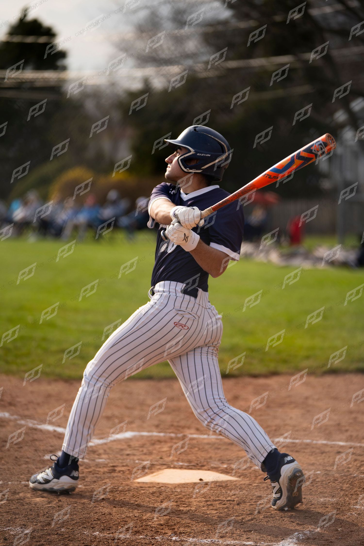 Baseball player in navy pinstripe uniform taking a full swing with an orange and blue bat.
