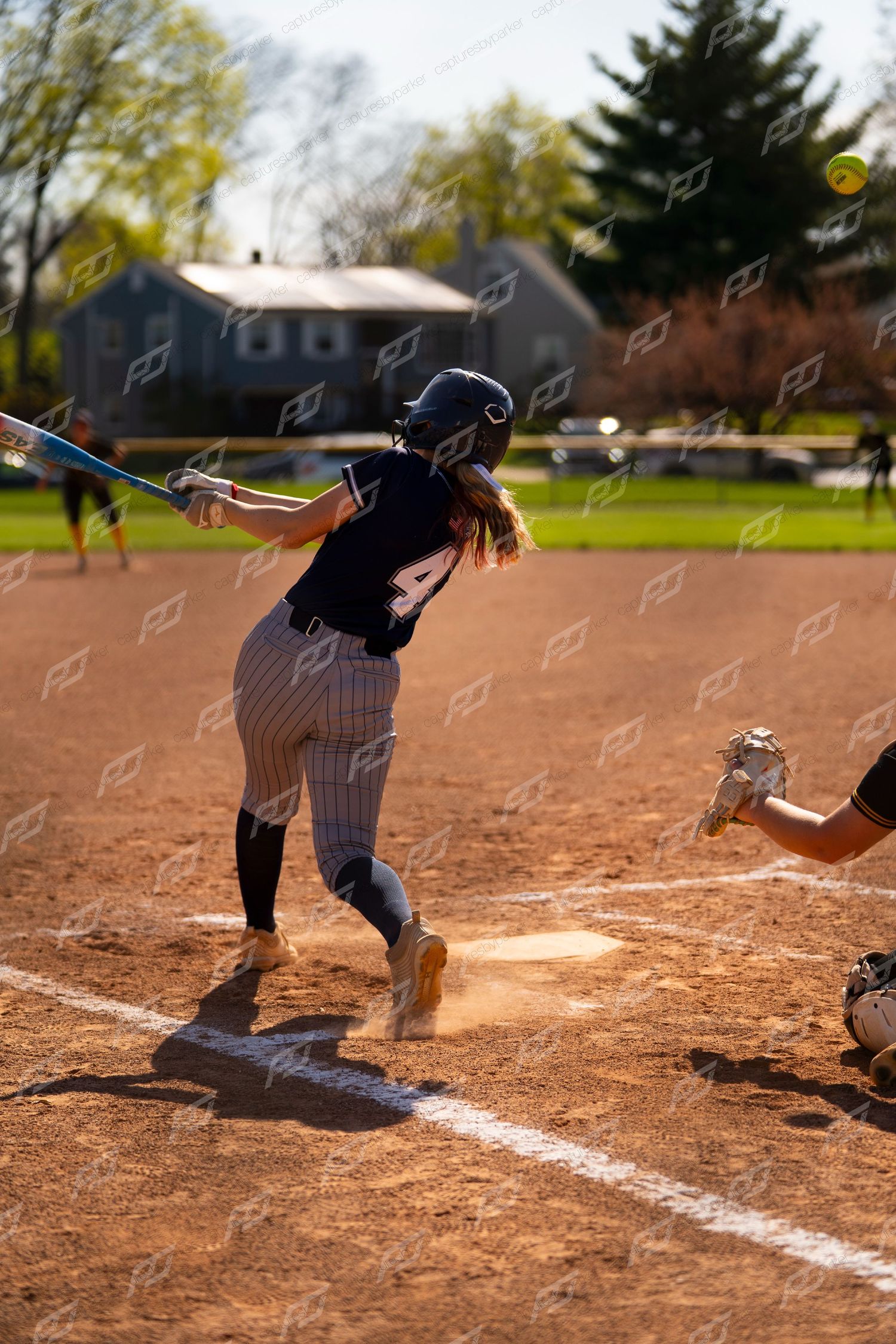 Softball batter in navy uniform swings at a pitch during a sunny game.