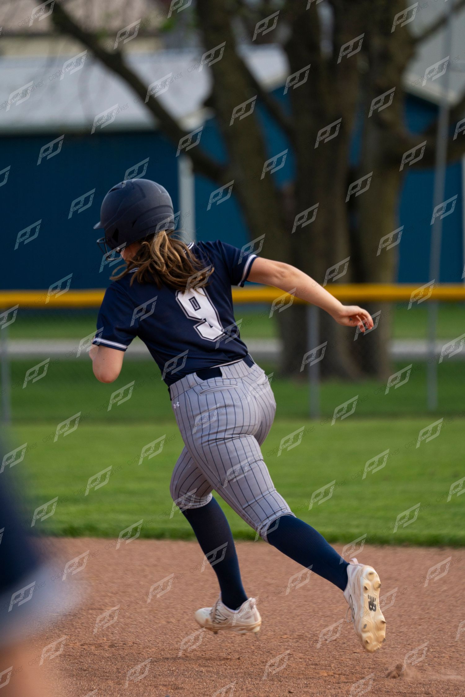 Female softball player number 9 in navy uniform sprints between bases.