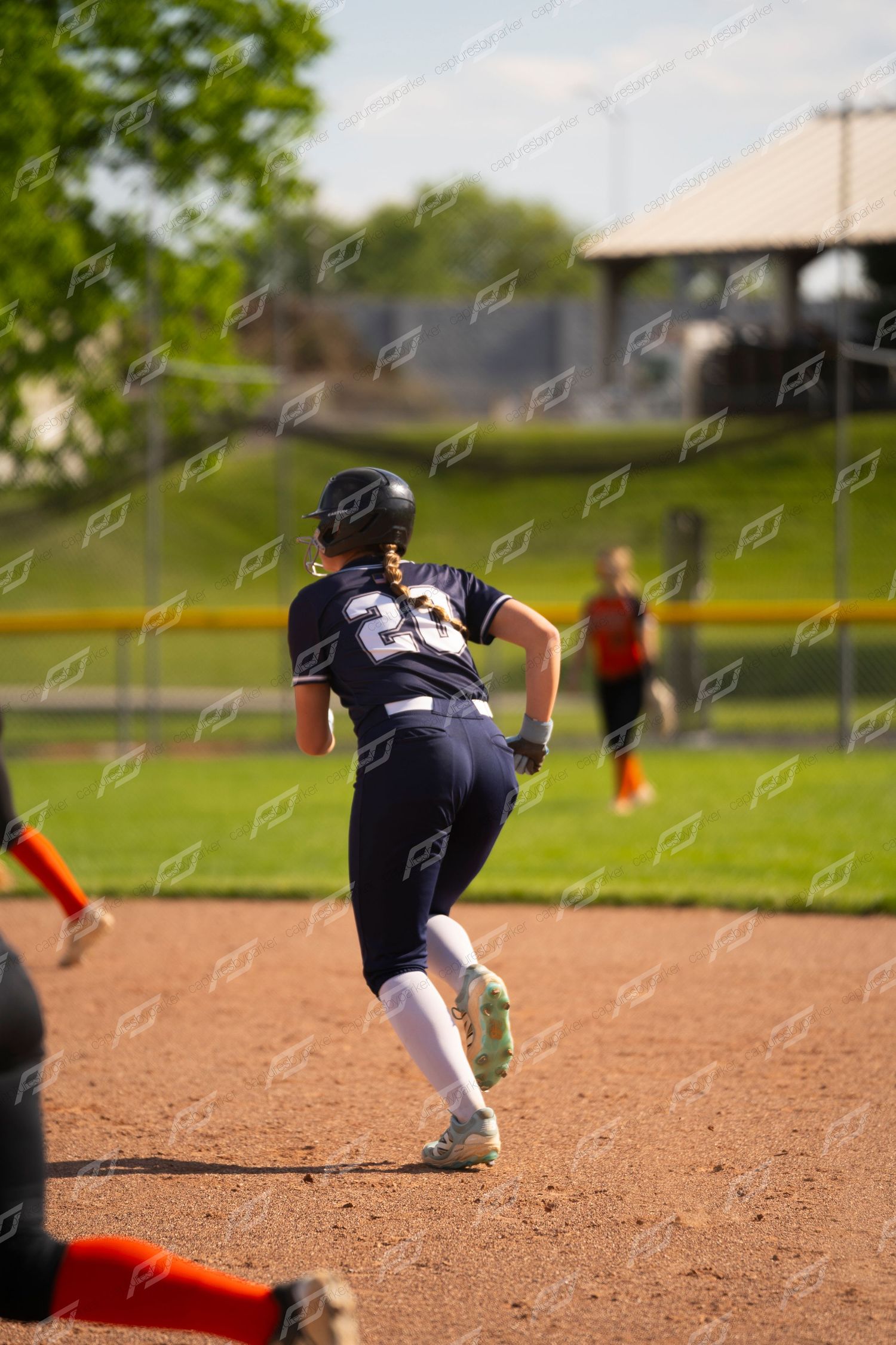 Youth softball player wearing number 23 runs bases during a sunny outdoor game.