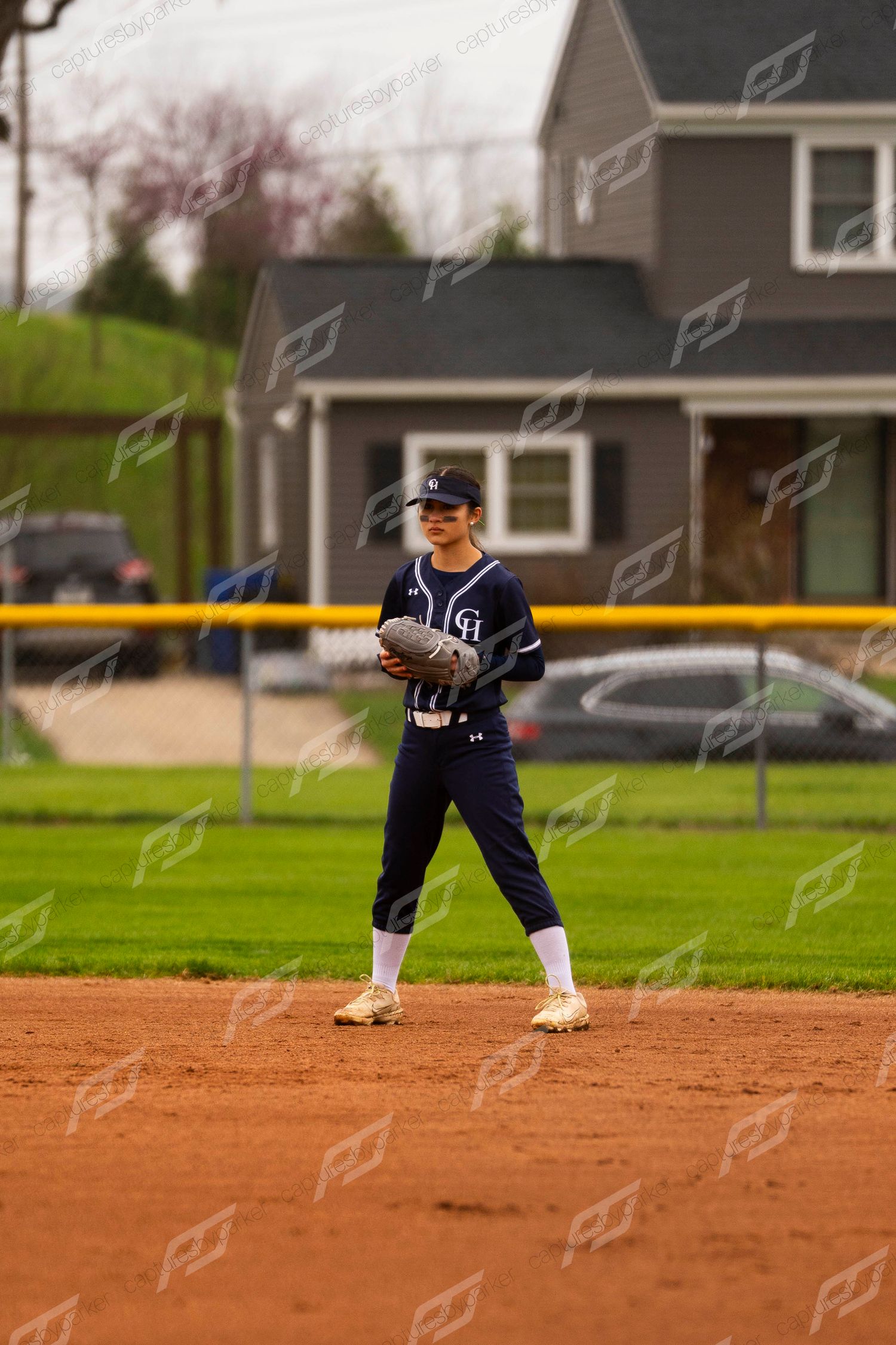 Female softball infielder in navy uniform standing ready on clay infield during a spring game.