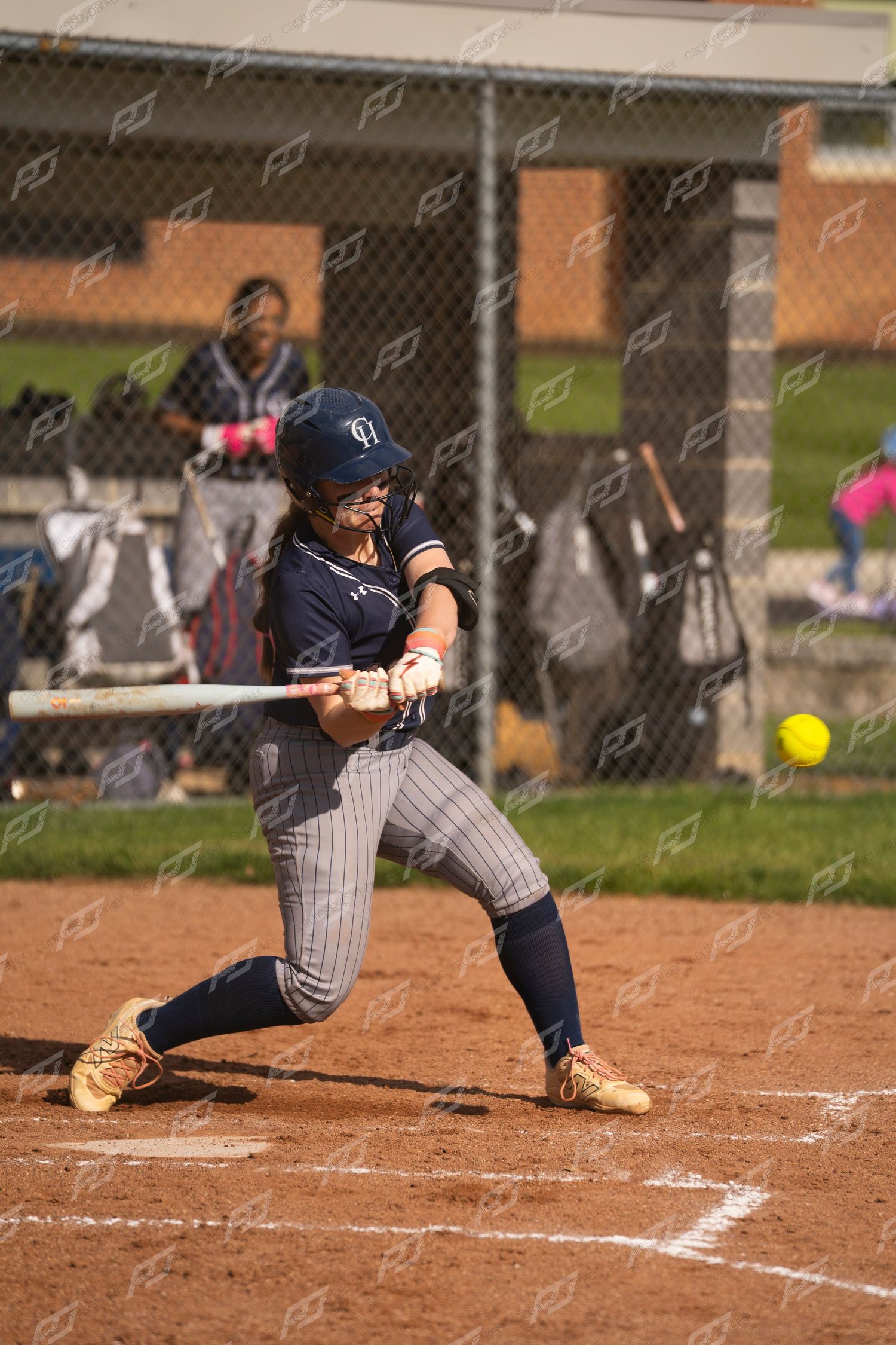 Female softball player in navy uniform makes contact with a yellow softball during an at-bat.