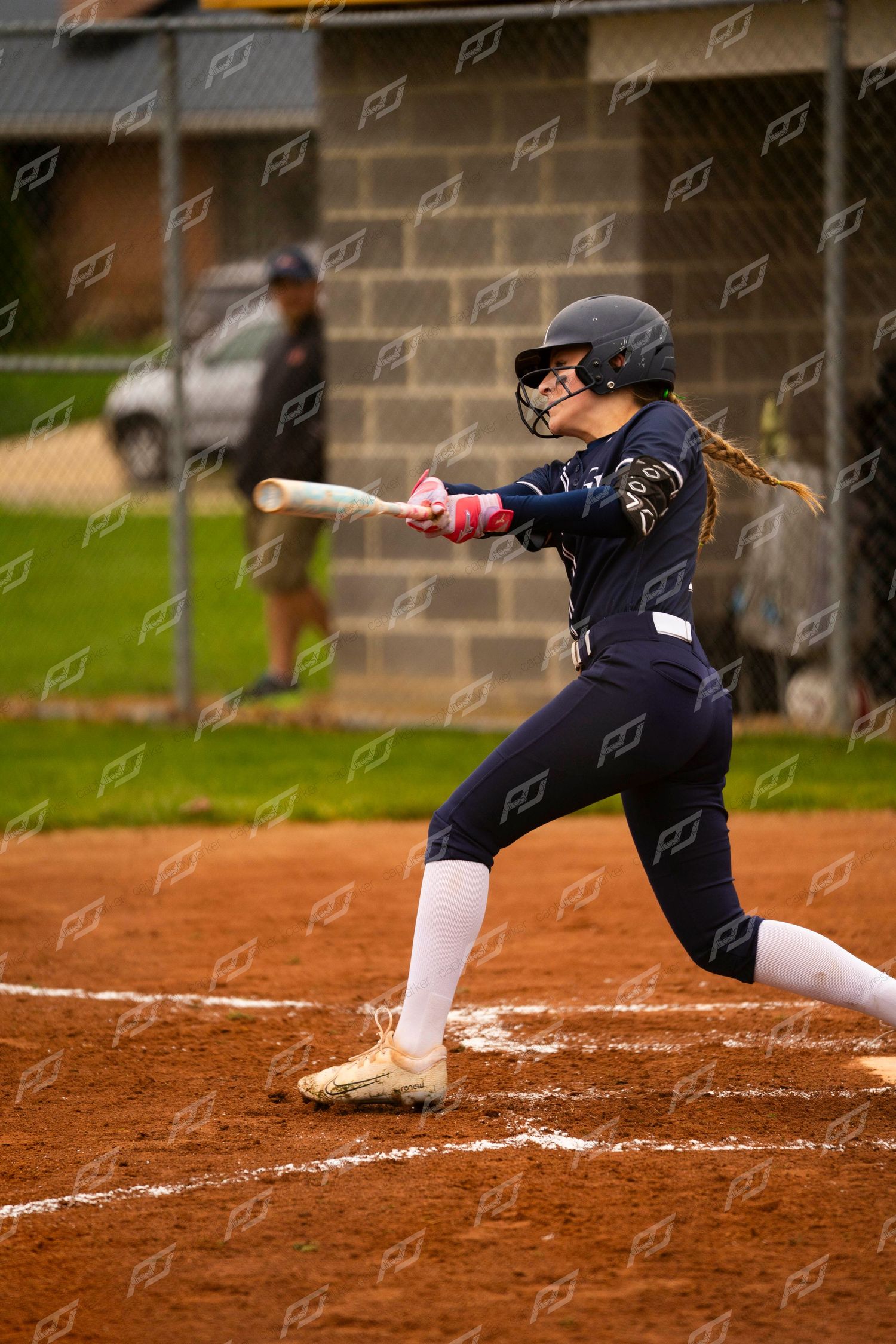 Female softball player in navy uniform makes contact hitting the ball at bat.