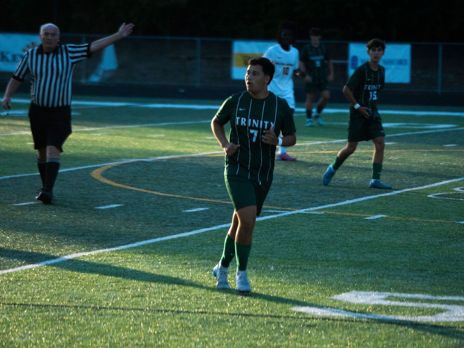 Trinity soccer player number 7 jogs on the field as a referee signals during a high school game.