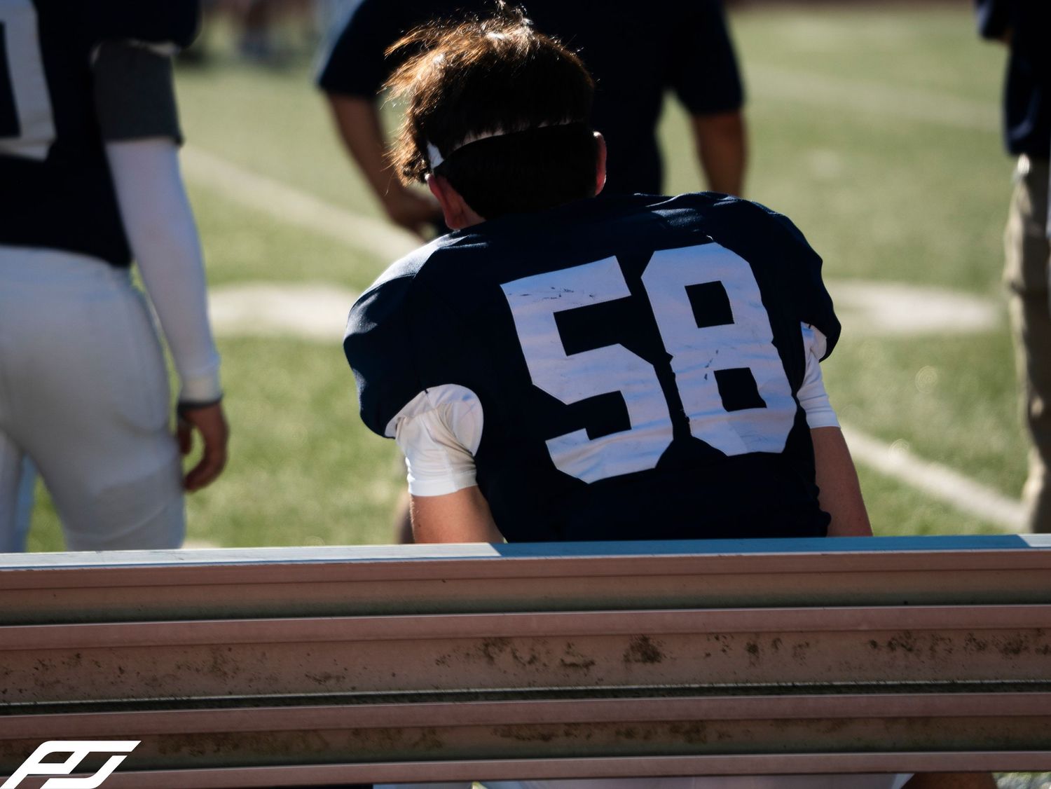 Youth football player wearing number 58 sits alone on the bench during a game.