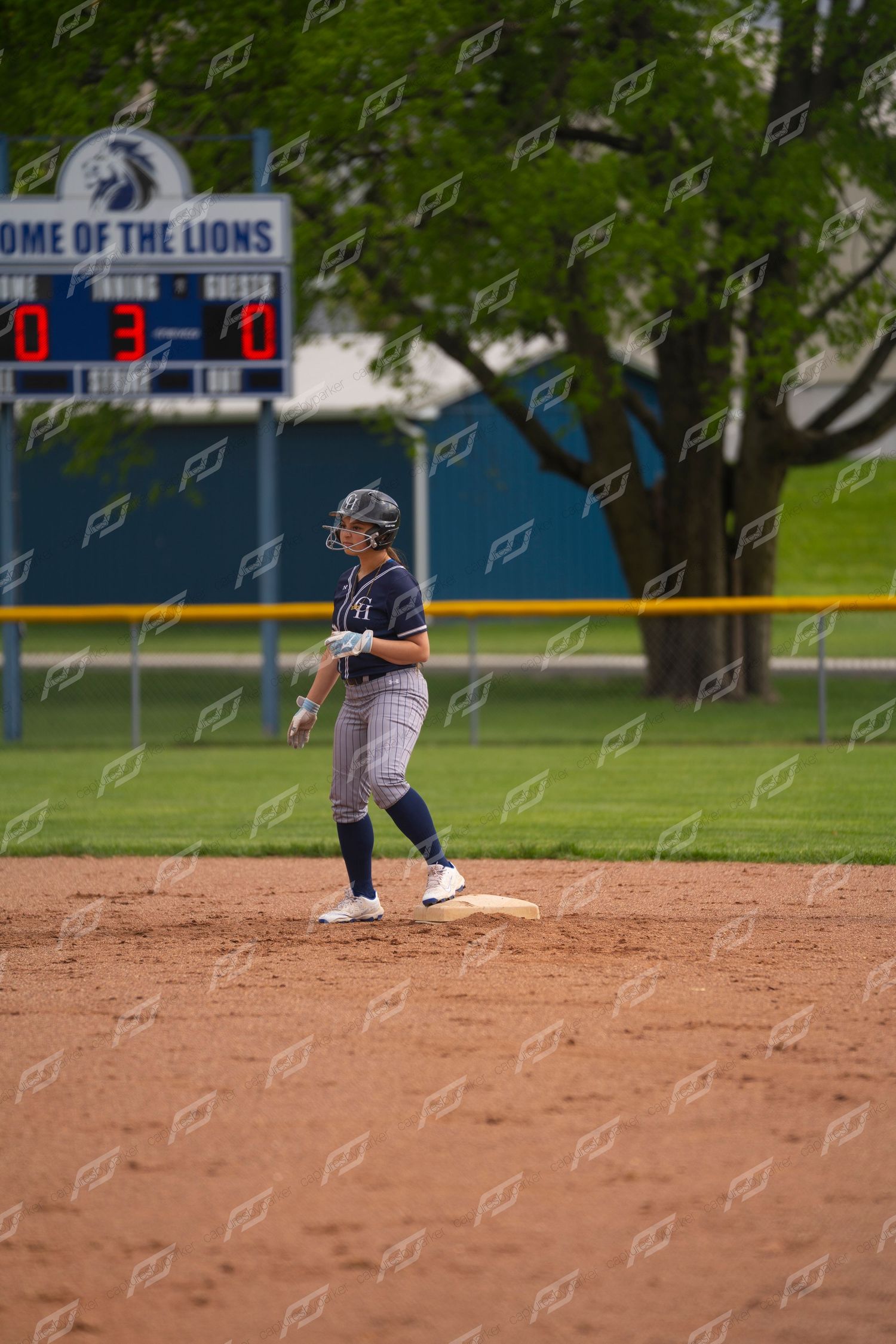 Softball player stands on second base with scoreboard reading 3-0 at Home of the Lions field.