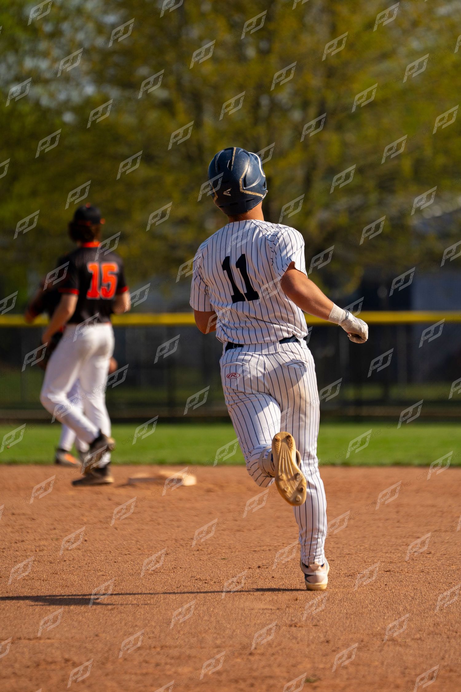 Baseball player #11 in white pinstripes rounds second base during a game with opponent #15 nearby.