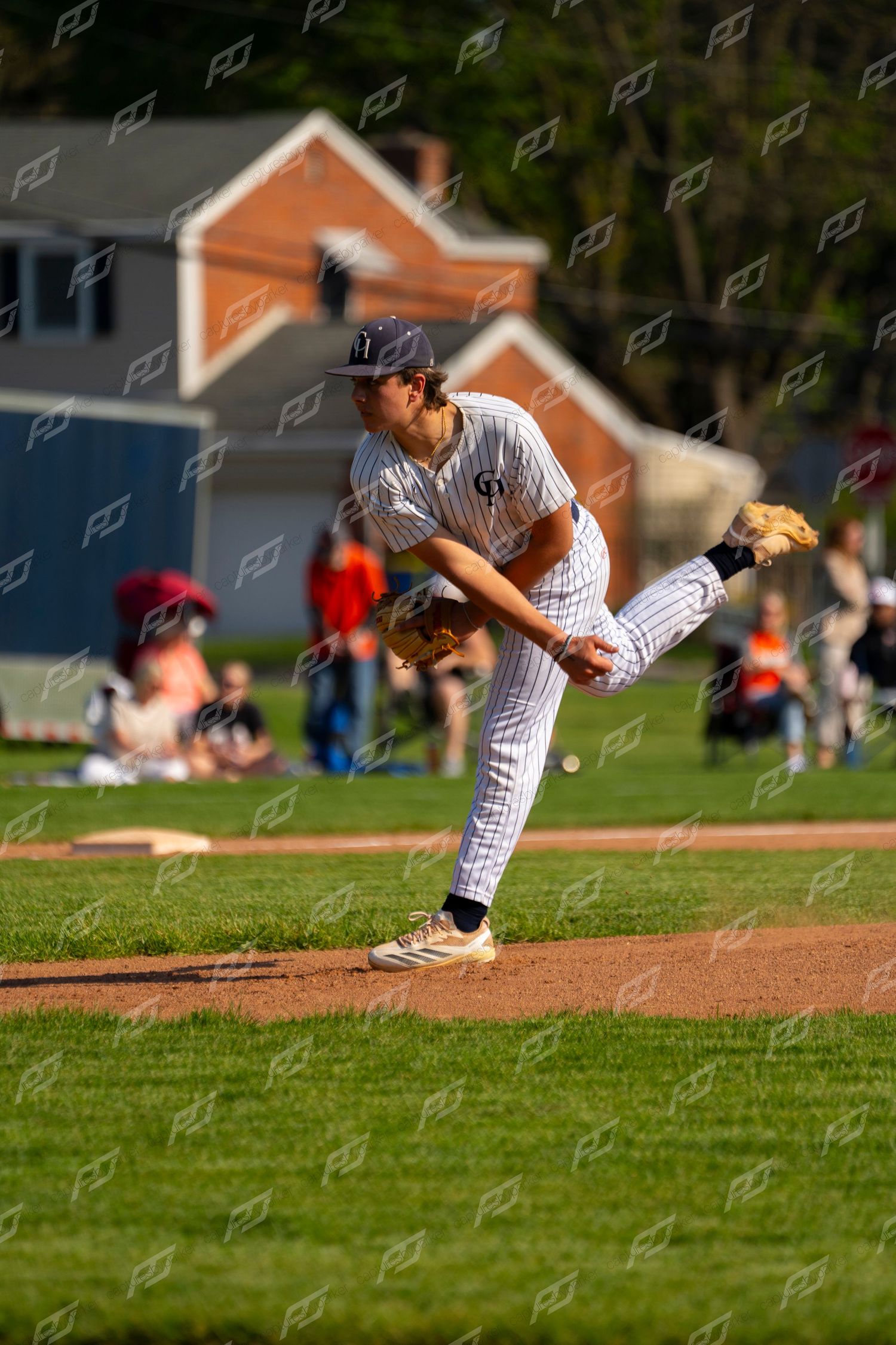 Baseball pitcher in white pinstripe uniform delivers a pitch from the mound during a sunny game.