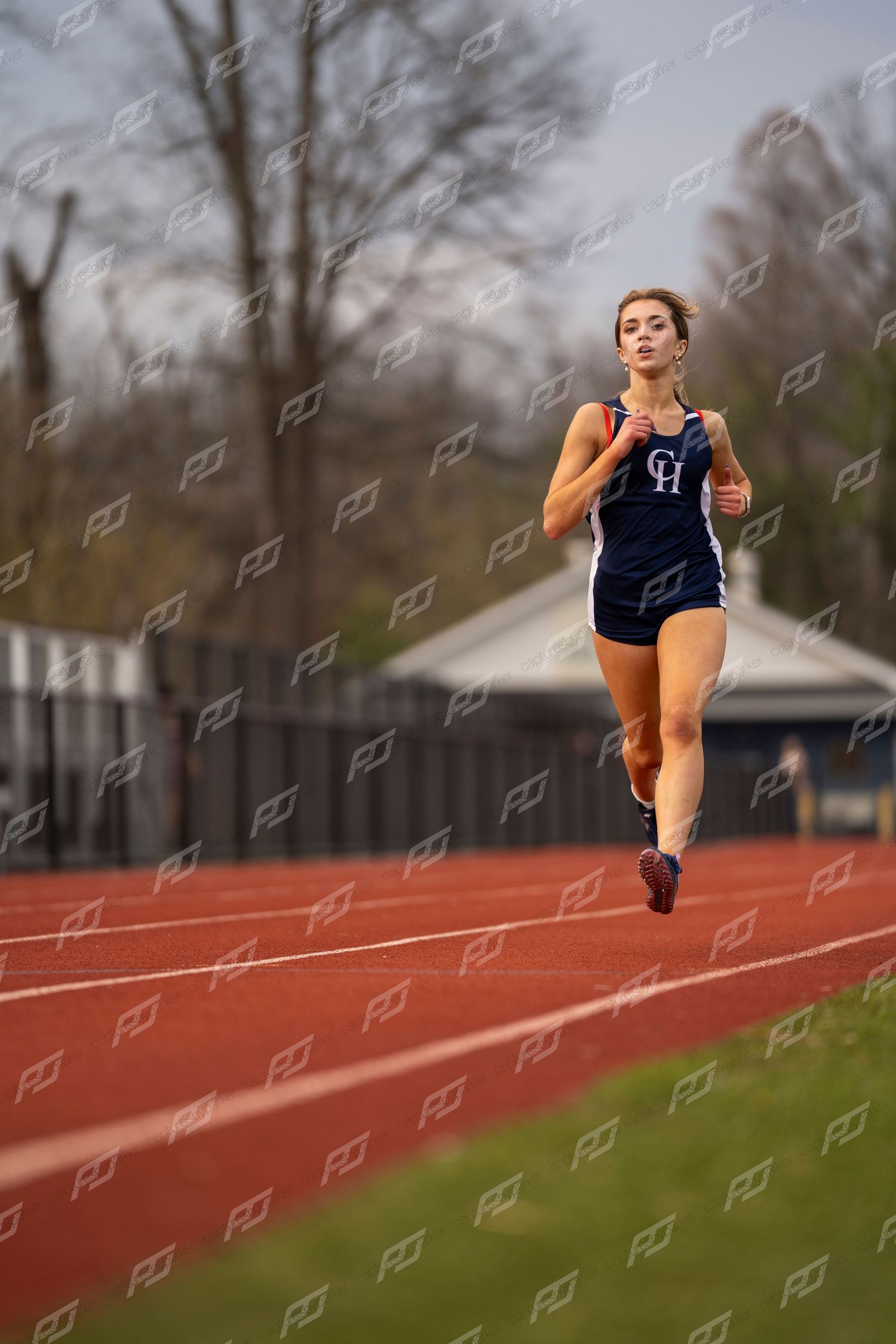 Female track athlete in navy CH uniform running alone on outdoor red track.