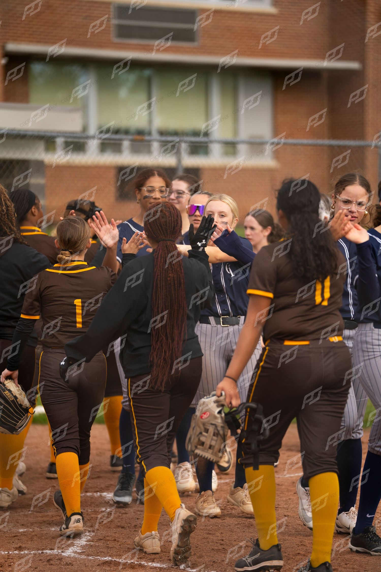 Softball players from two teams celebrate and take photos in a post-game handshake.