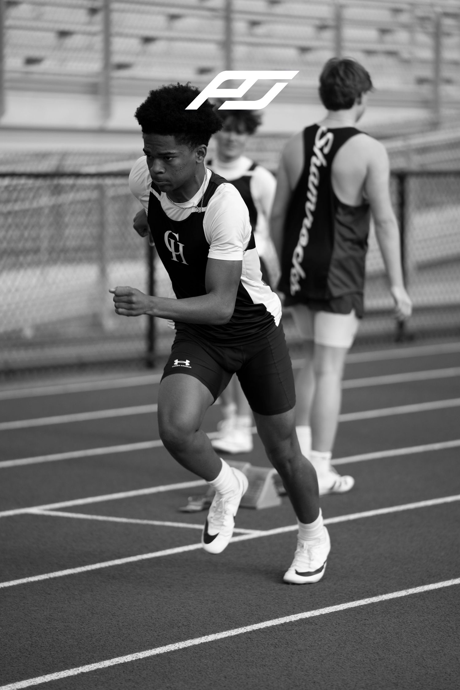 Black and white photo of a young male sprinter in a CH track uniform exploding off the starting line on an outdoor track.