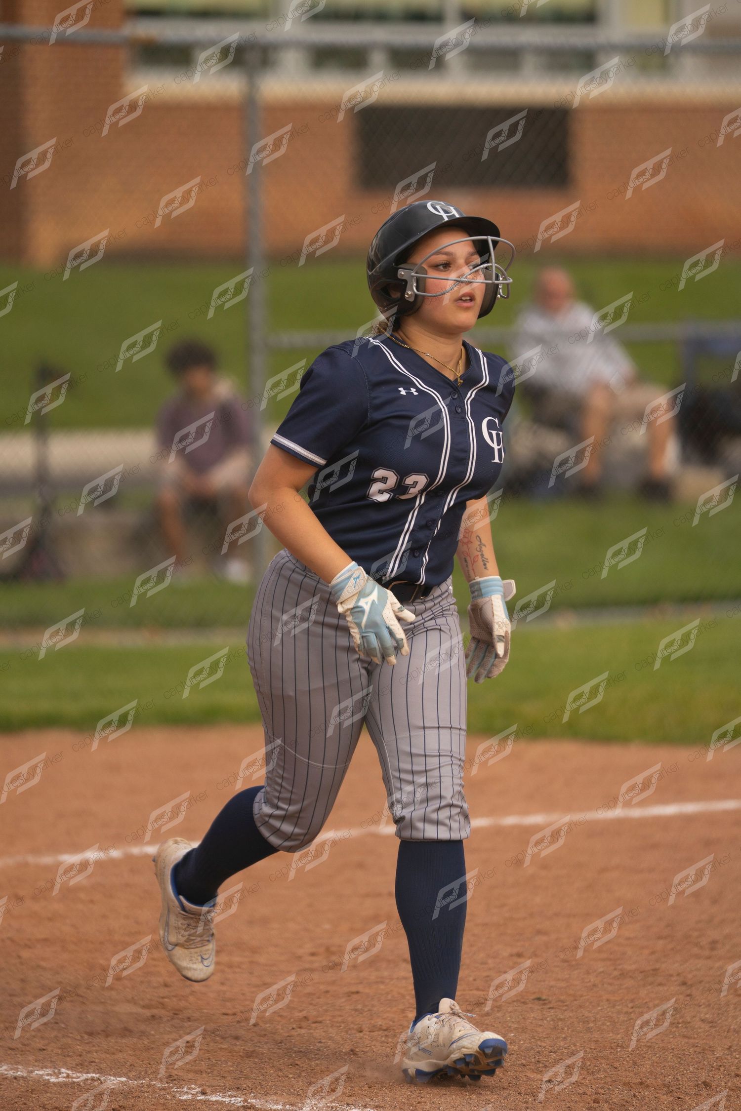 Softball player #23 in navy pinstripe uniform running toward first base during game.