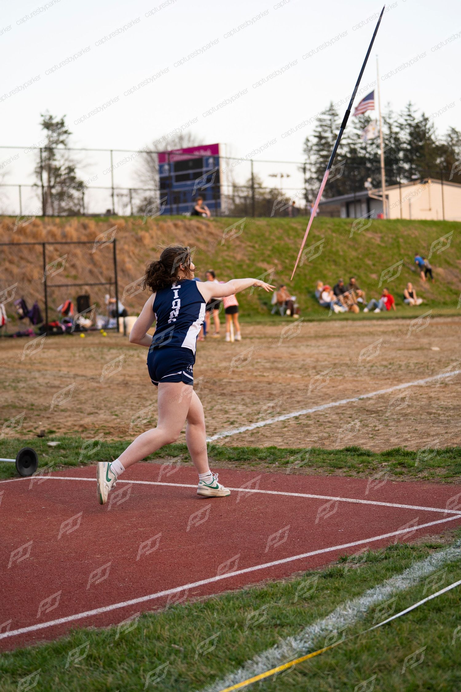 Young female athlete throws javelin on red track during outdoor high school track and field meet.