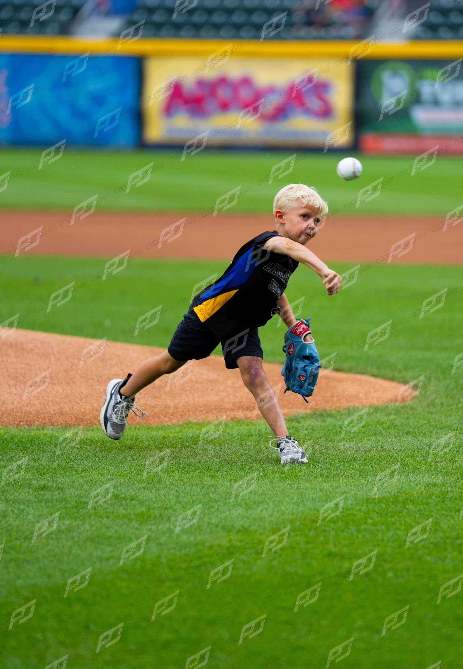 Young blonde boy throwing a ceremonial first pitch on a baseball field during a minor league game.