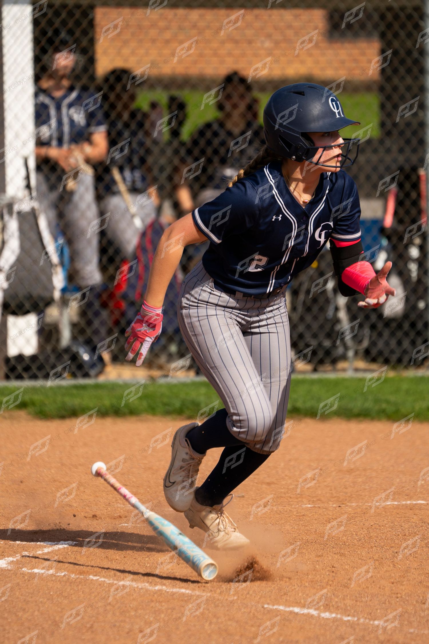 Female softball batter in navy uniform drops bat and runs to first base after hitting pink ball.