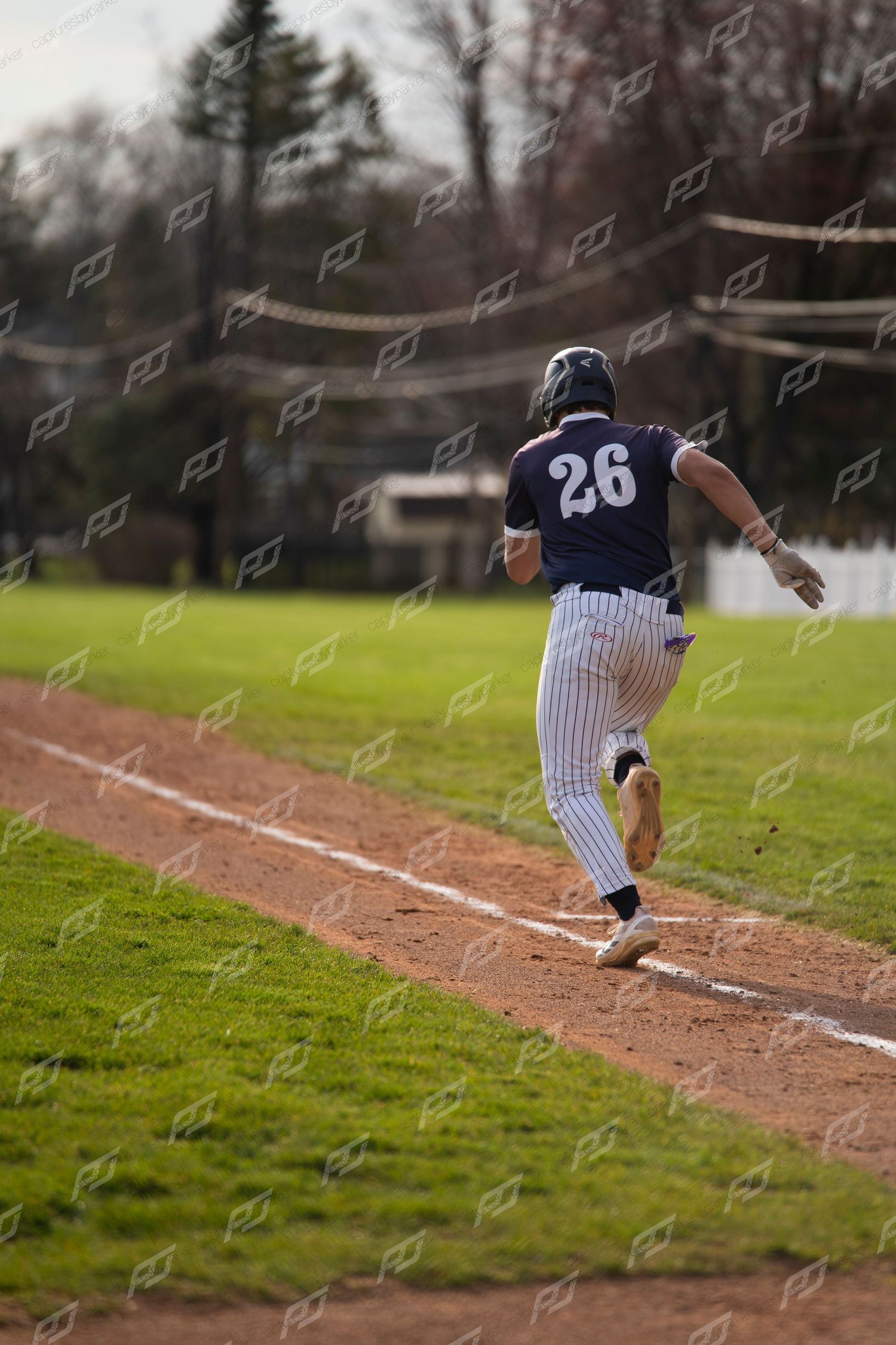 Baseball player #26 runs the base line during an outdoor game on a sunny day.