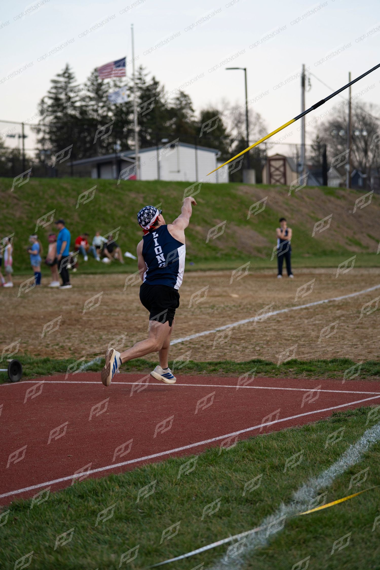 Male Lions athlete mid-throw releasing javelin at outdoor track event.