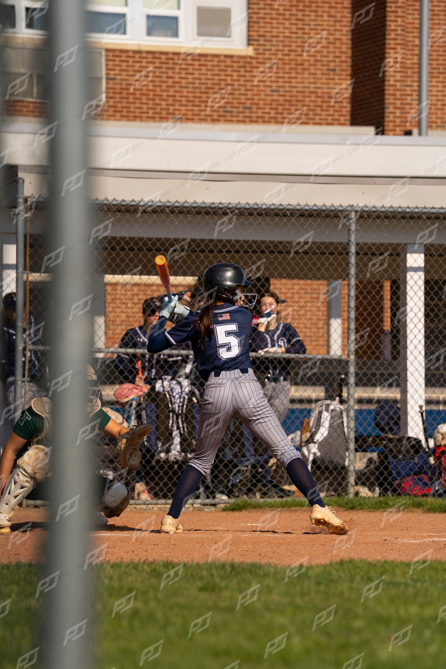 Female softball player number 5 in navy uniform at bat during a competitive softball game.