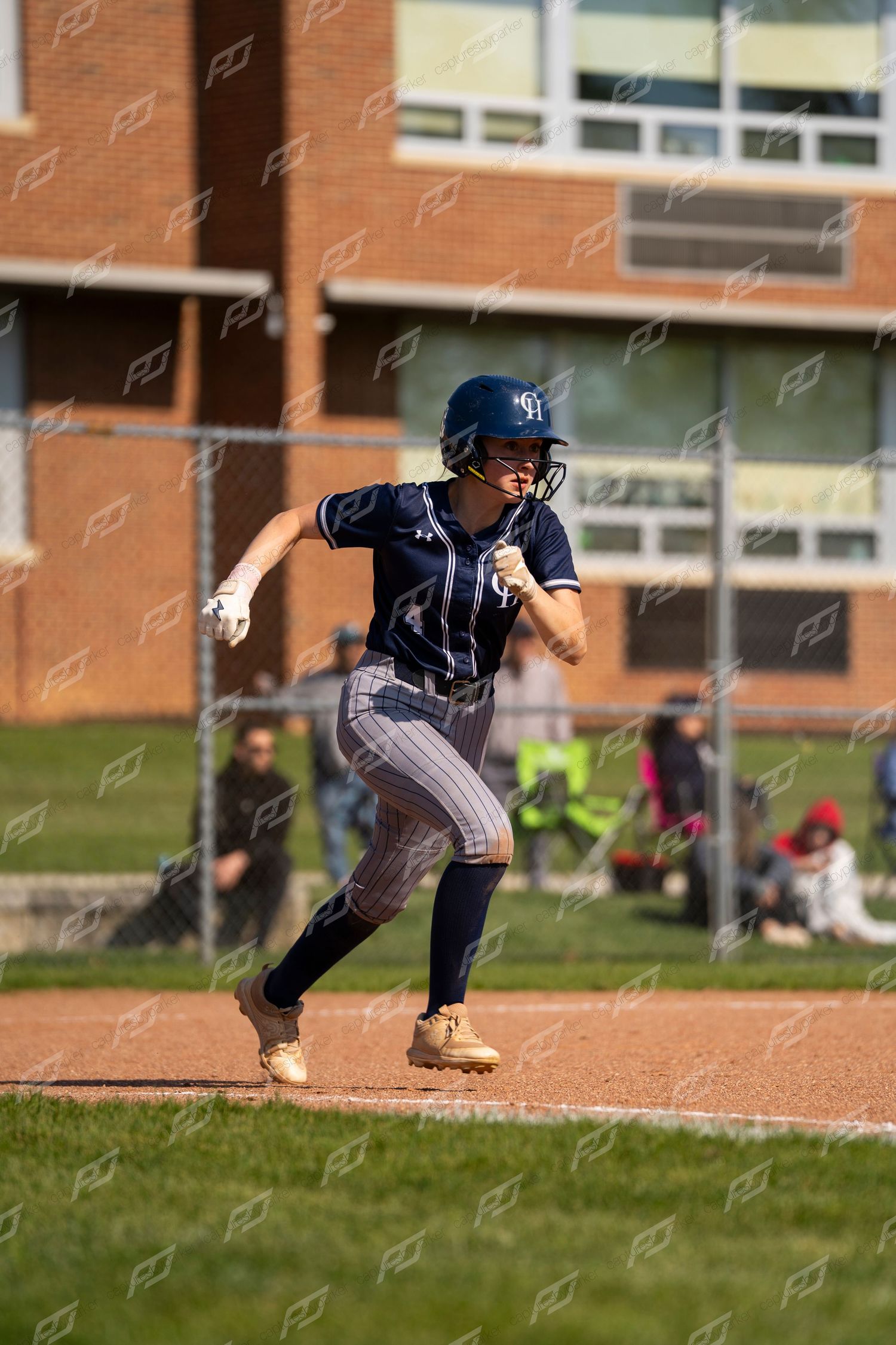 Female softball player in navy pinstripe uniform sprints toward base during game.