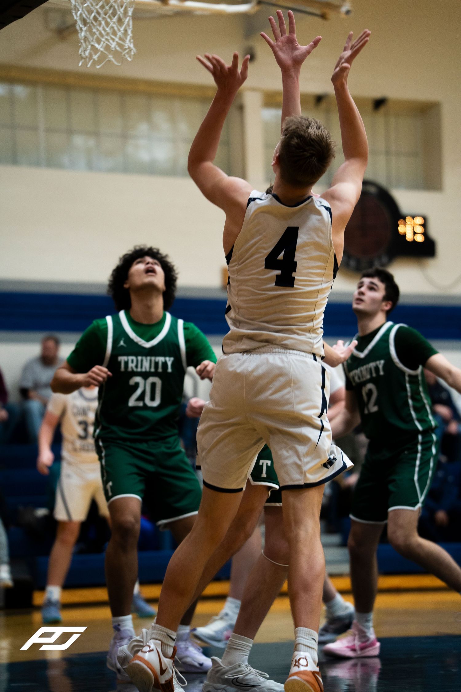 Camp Hill Lions player #4 reaches for rebound against Trinity Crusaders defenders #20 and #2 in green uniforms.