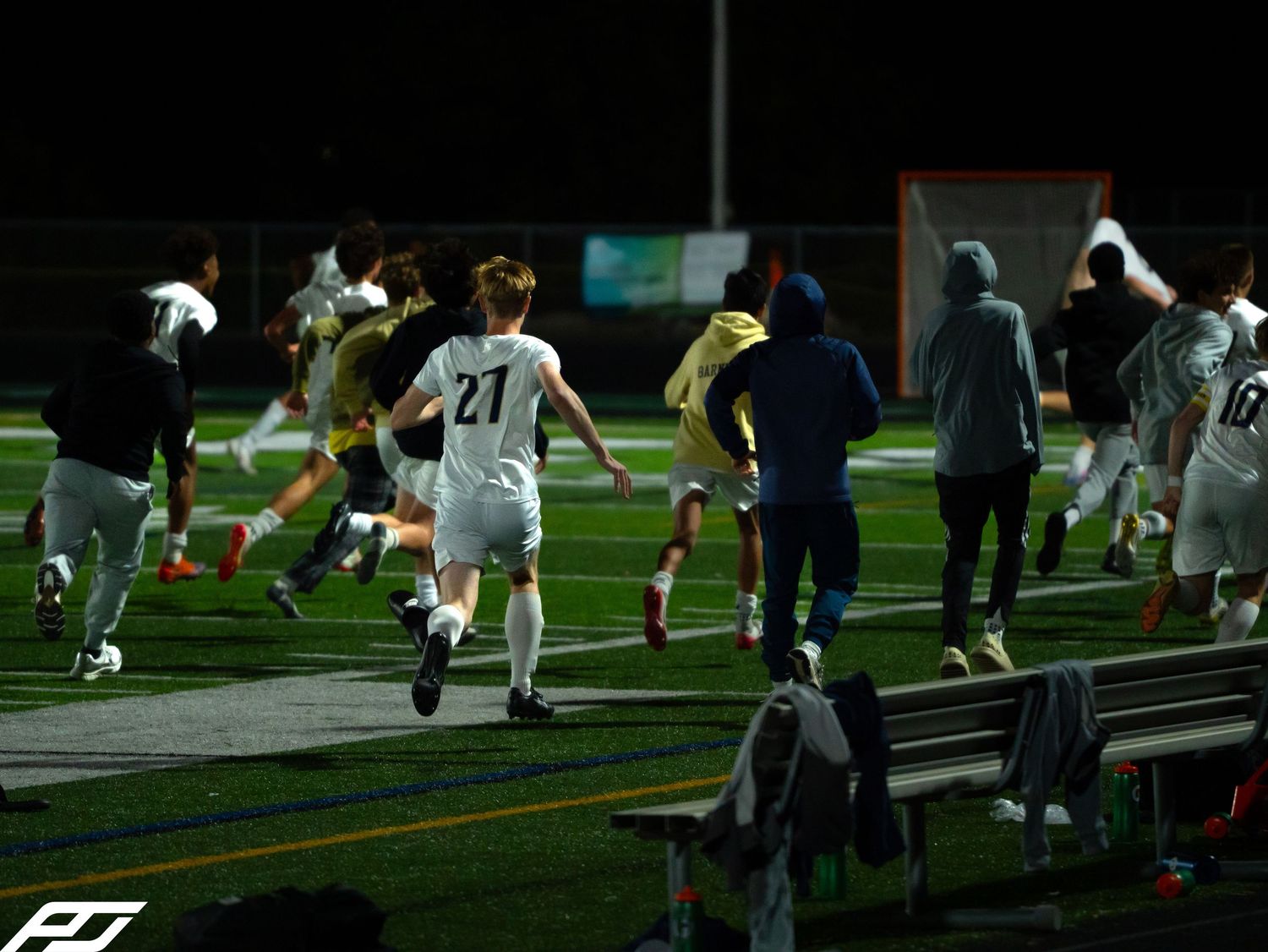 Soccer players and coaches rushing onto the turf field during a night game.