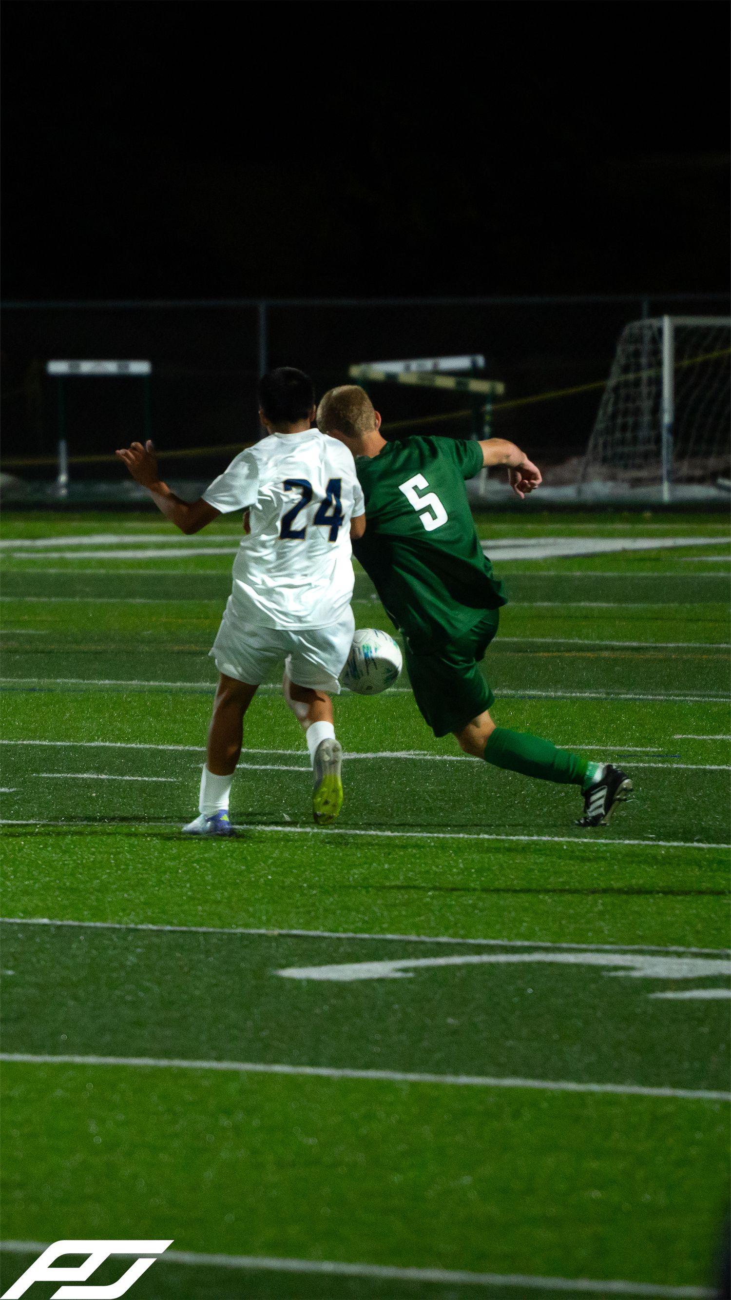 Soccer player #5 in green battles for the ball against opponent #24 in white during a night game.