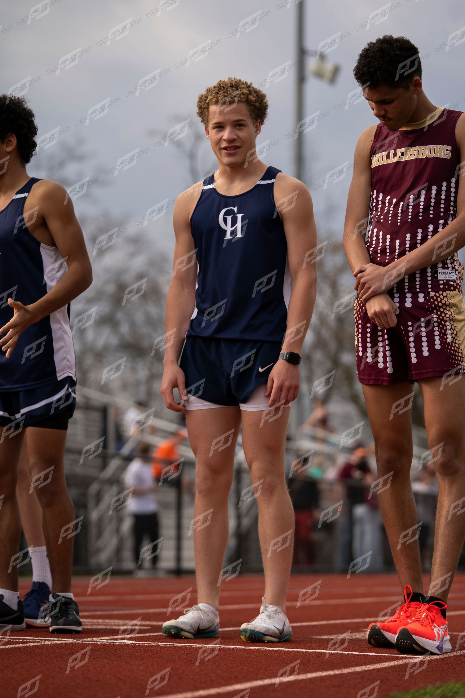 Male CH track athlete in navy uniform standing at starting line with competitors.