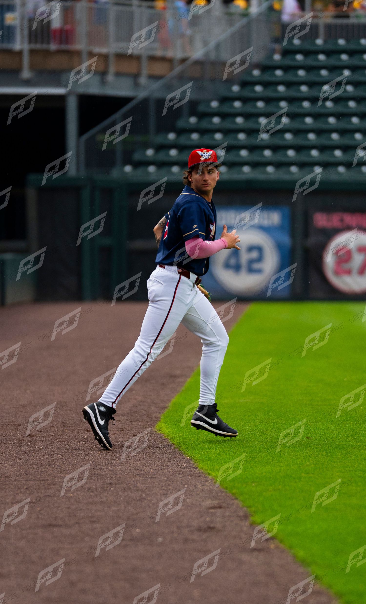 Minor league baseball player in navy uniform jogging along the warning track near the dugout.