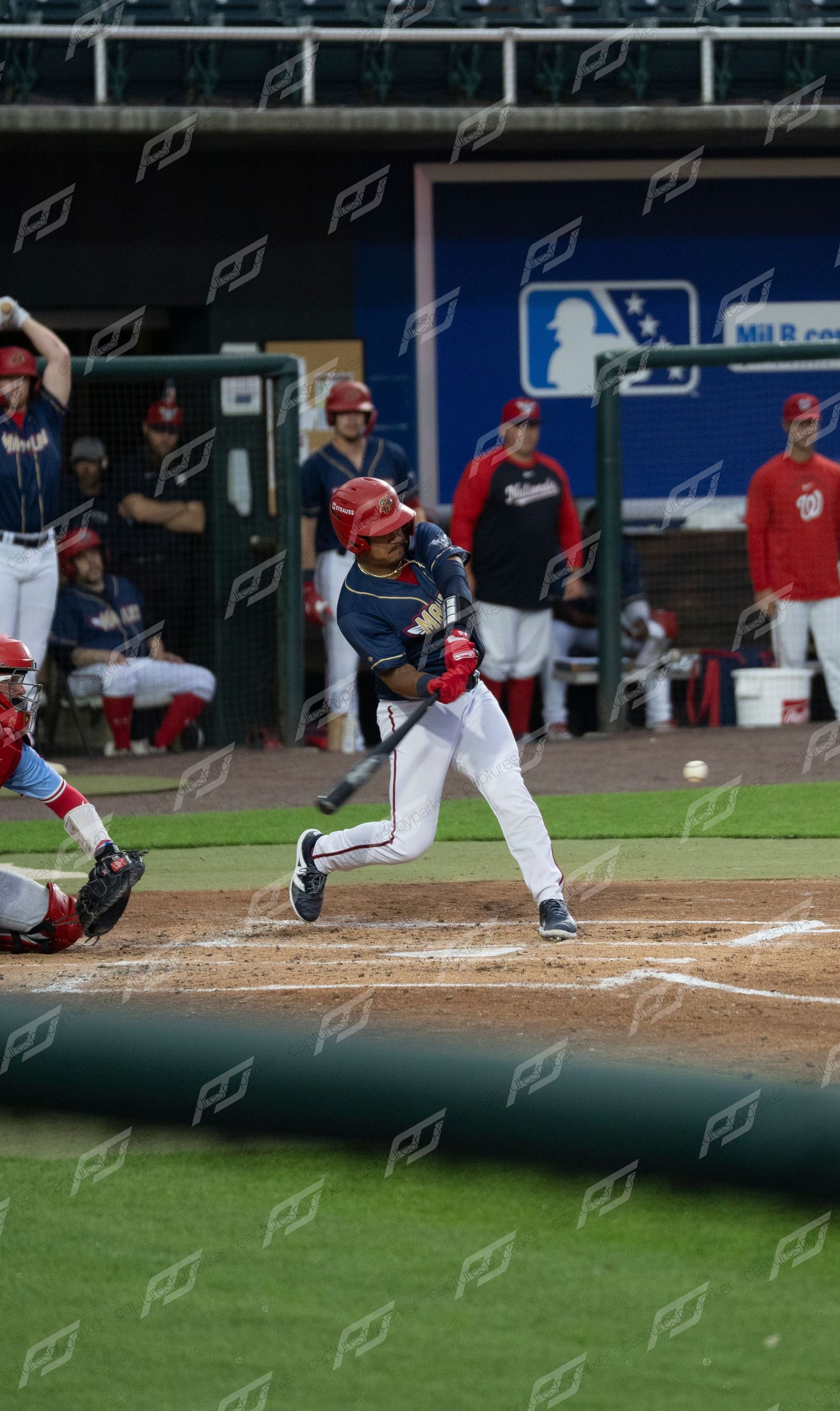 Minor league batter in navy uniform swings at low pitch as catcher reaches for ball during game.