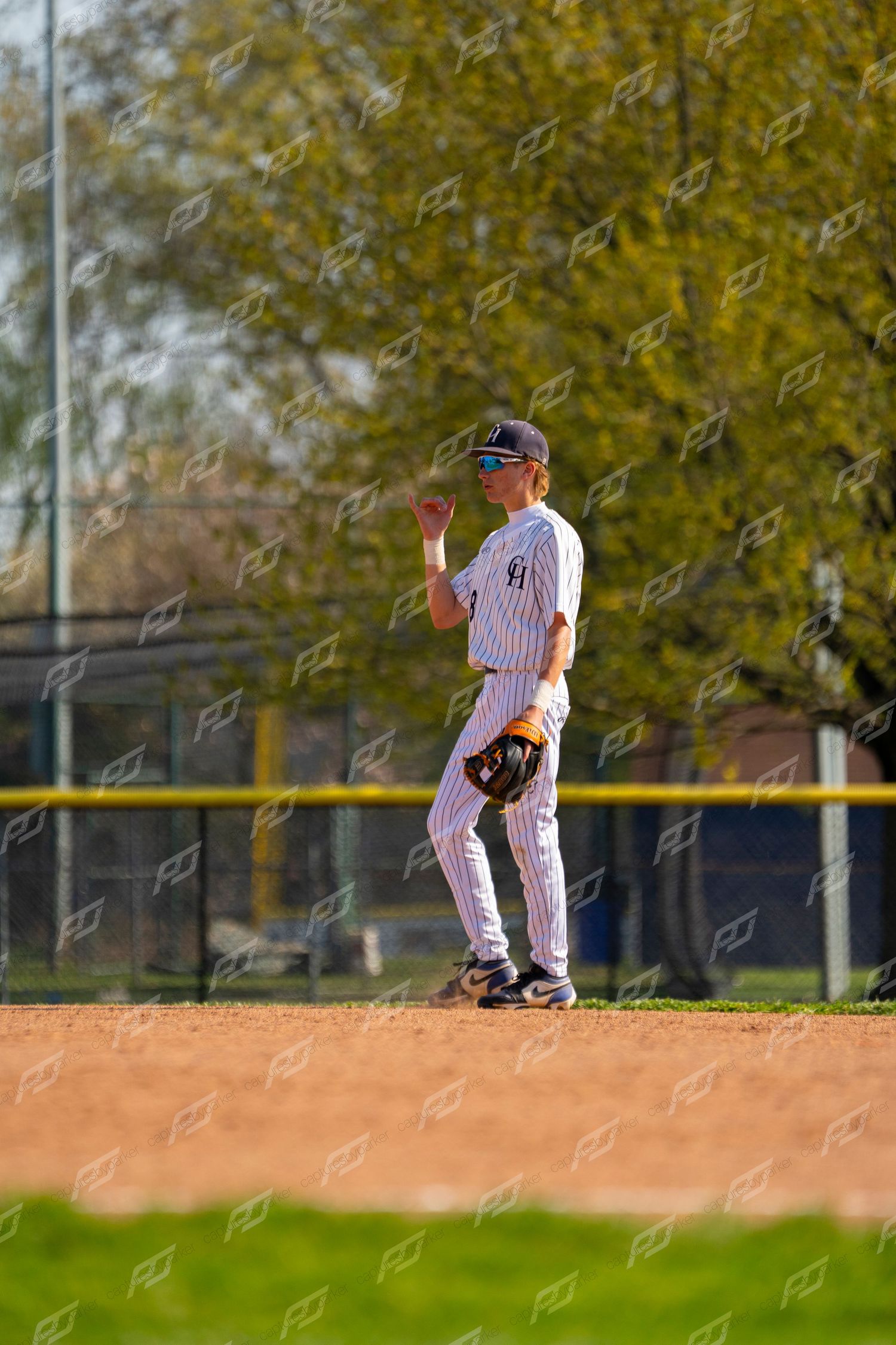 Baseball infielder in pinstripe uniform signals with glove raised on sunny field.