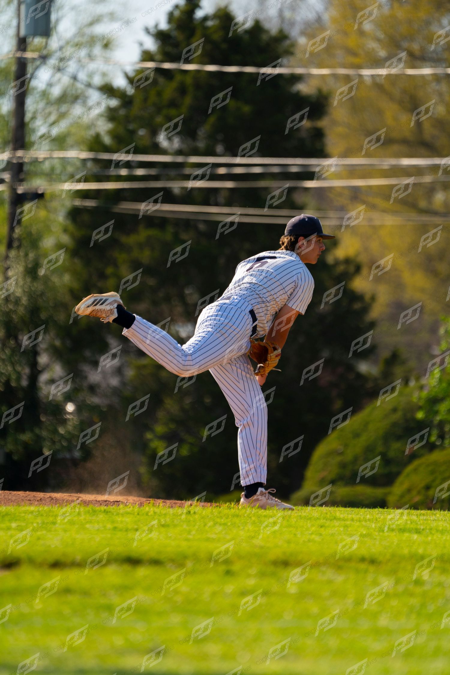 Baseball pitcher in white pinstripe uniform follows through on a pitch during an outdoor game.