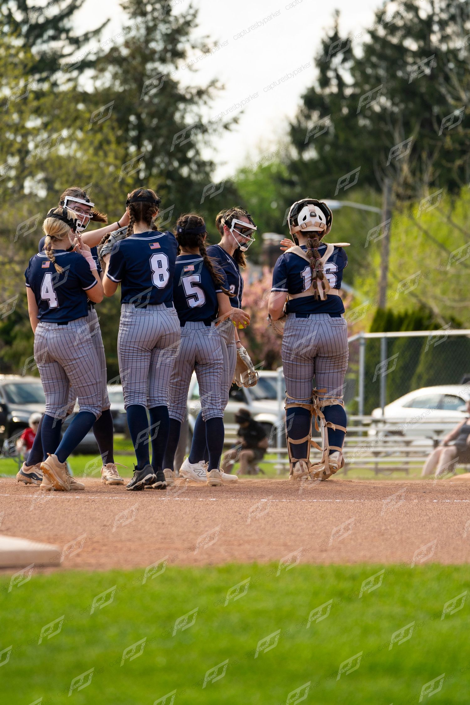 Female softball team in navy pinstripe uniforms huddles together on infield dirt during game timeout.