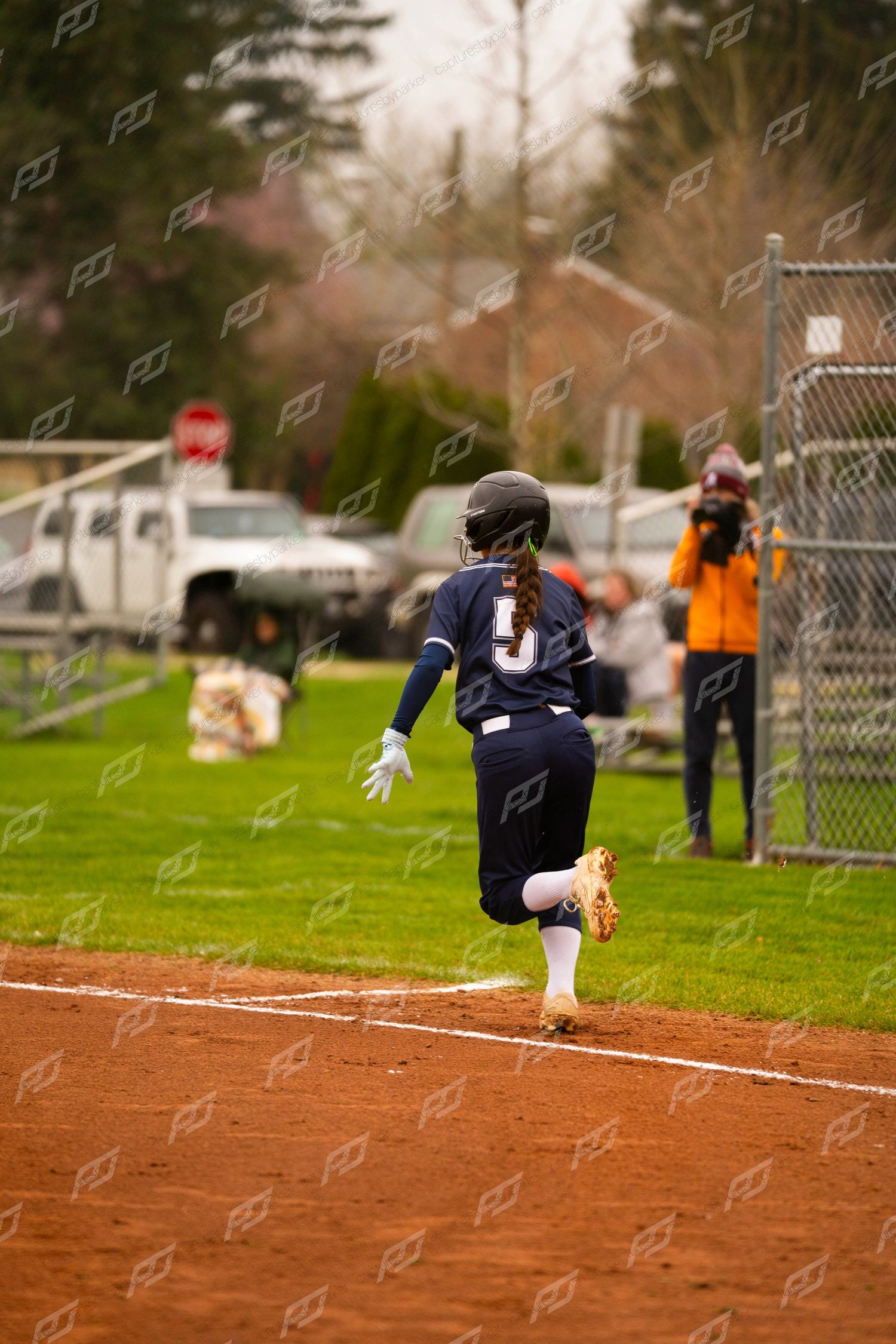 Female softball player #5 in navy uniform sprints down the baseline during a game.