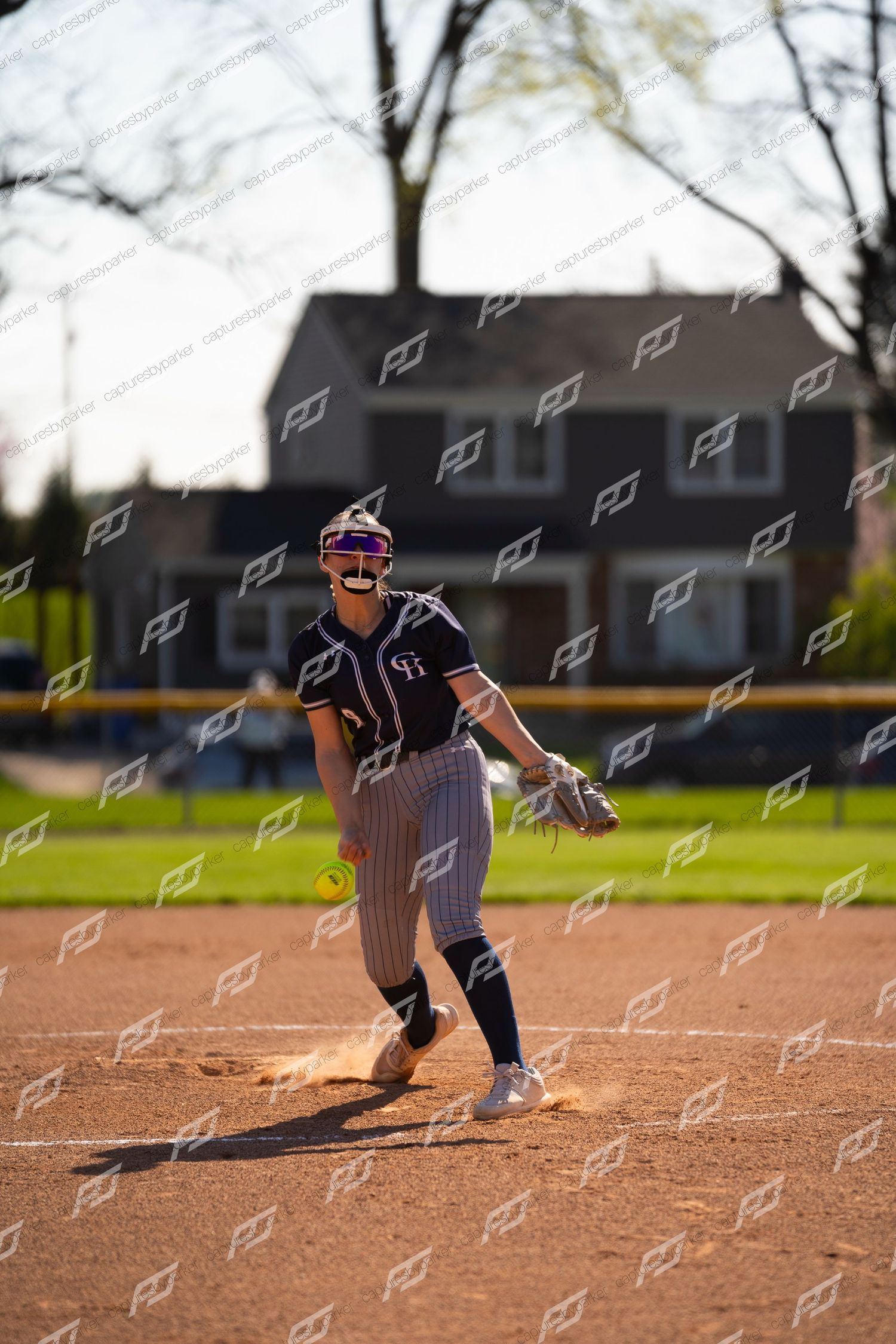 Female softball pitcher winds up for a pitch in navy pinstripe uniform outdoors.
