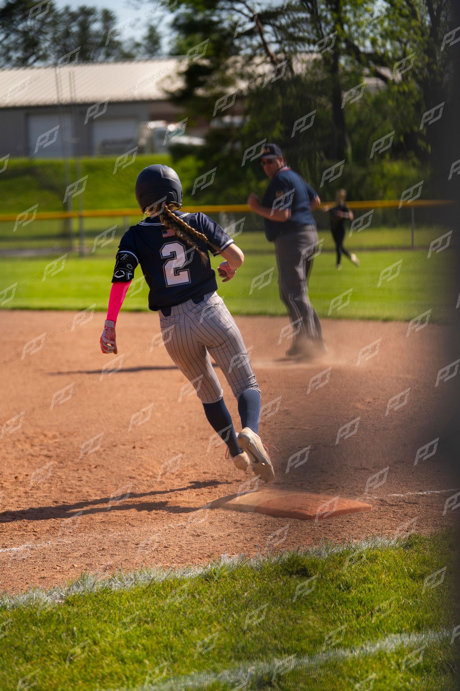 Youth softball player #2 rounds a base in a cloud of dust during an outdoor game.
