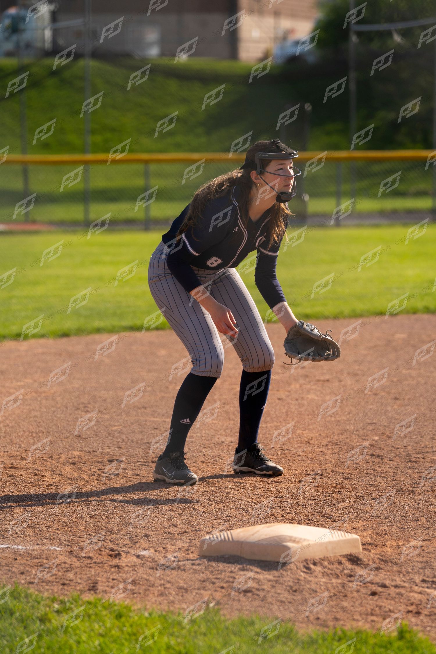 Female softball player in dark uniform crouching in fielding position at a base during a game.