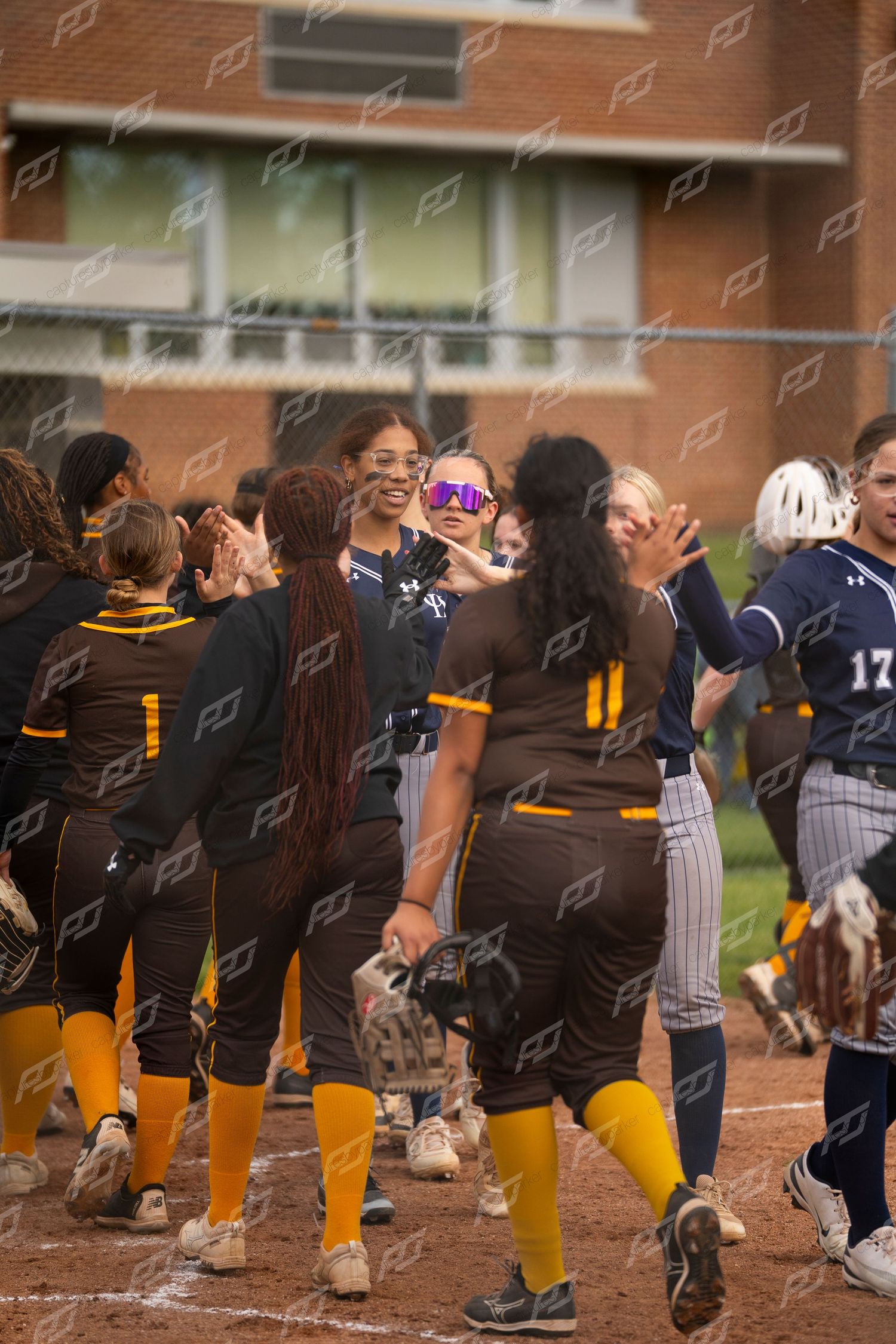 Smiling softball players high-five opponents in a post-game sportsmanship handshake line.