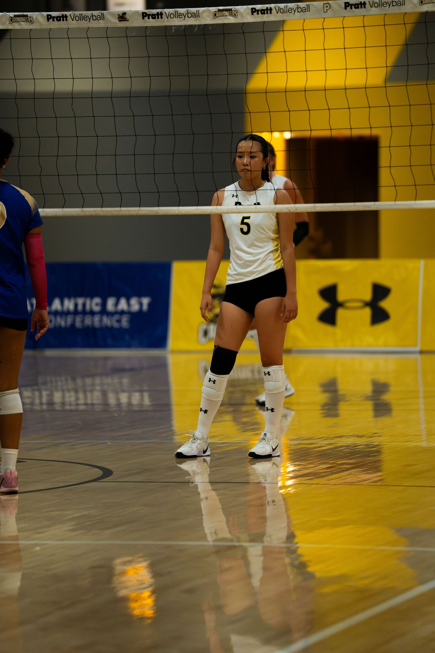 Female volleyball player wearing number 5 jersey stands ready on indoor court during Atlantic East Conference match.