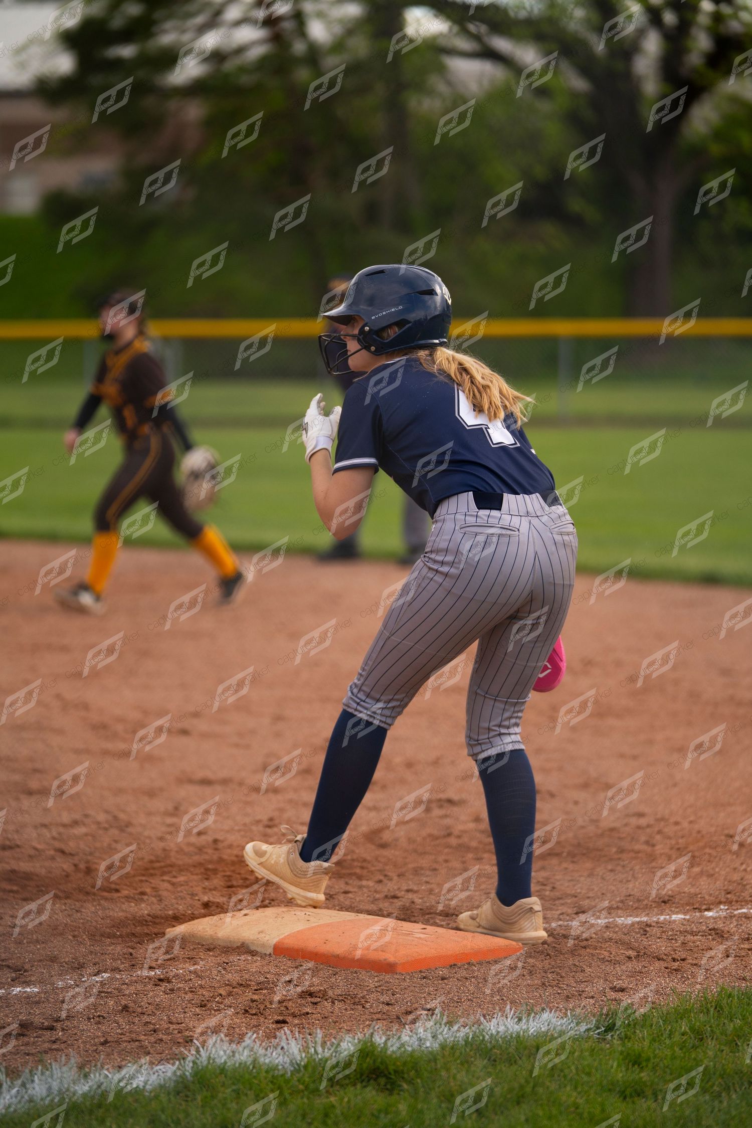 Softball player stands on an orange base ready to advance during a game.