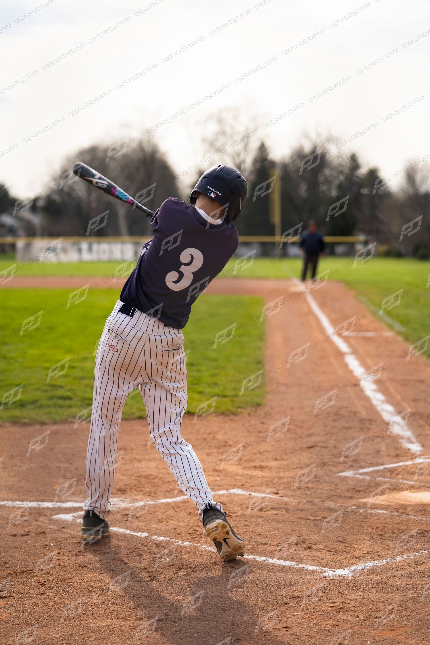 Baseball player #3 in navy uniform winds up for a swing at home plate on a dirt infield.