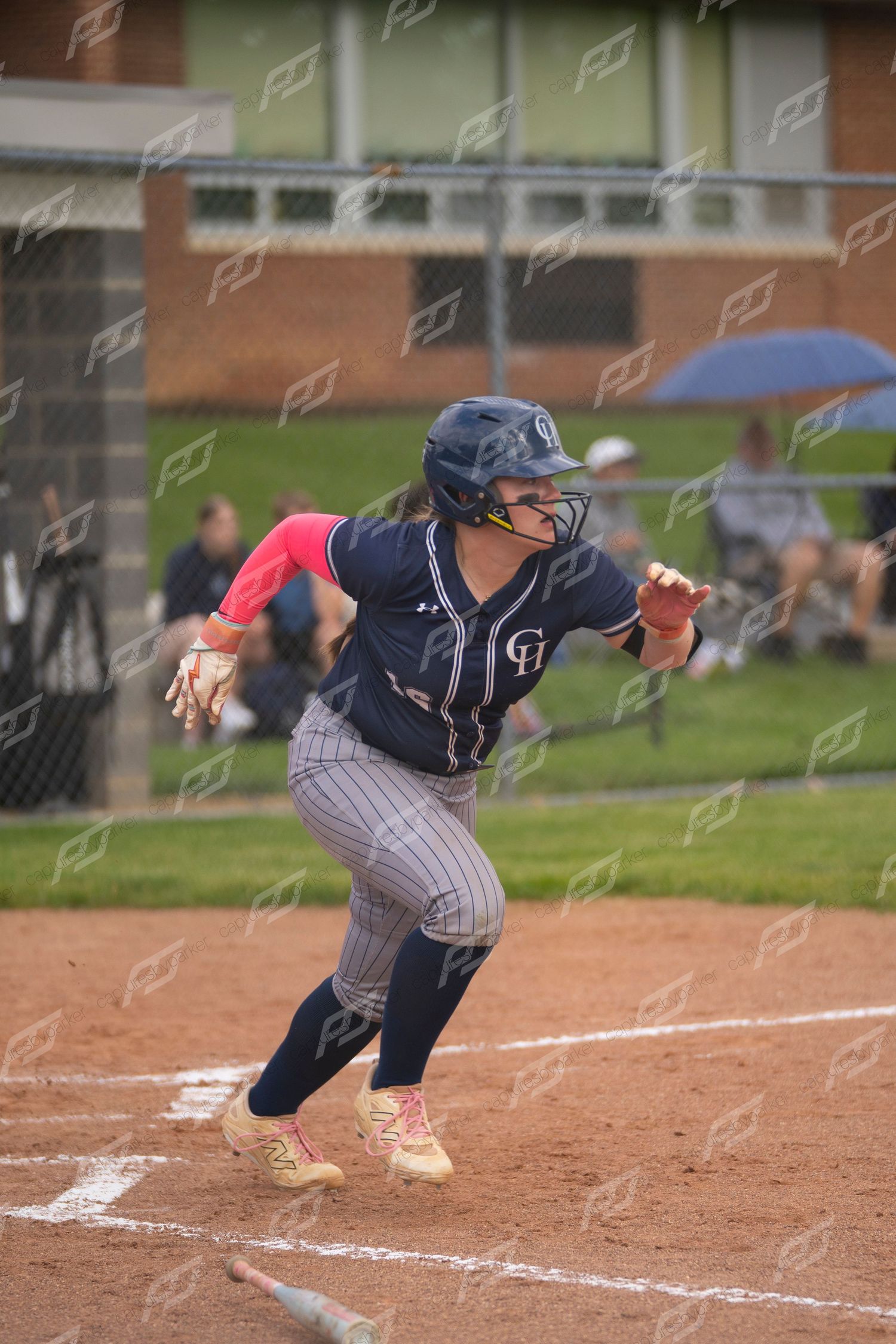 Female softball player in navy uniform crouches in batting stance ready to run the bases.