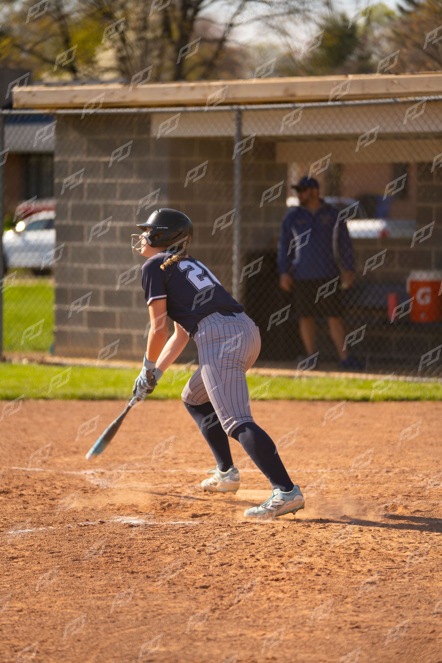Female softball player #20 in navy pinstripe uniform following through on swing at home plate.