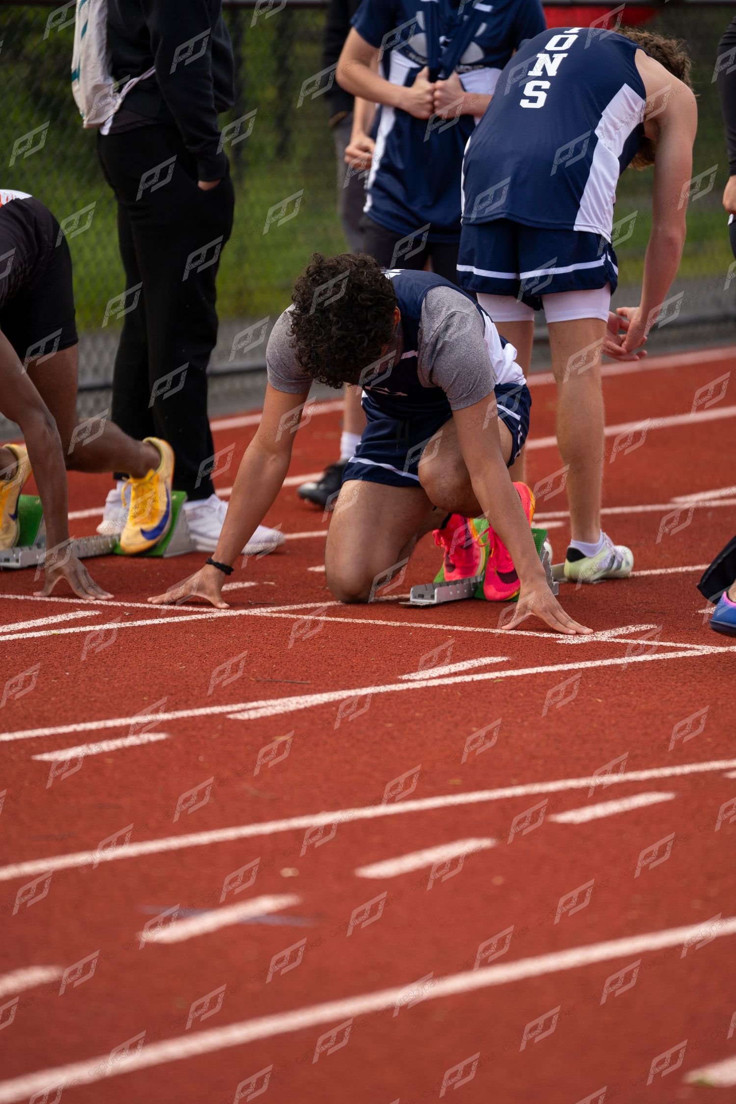 Male sprinter in starting position on red track at outdoor high school track meet.