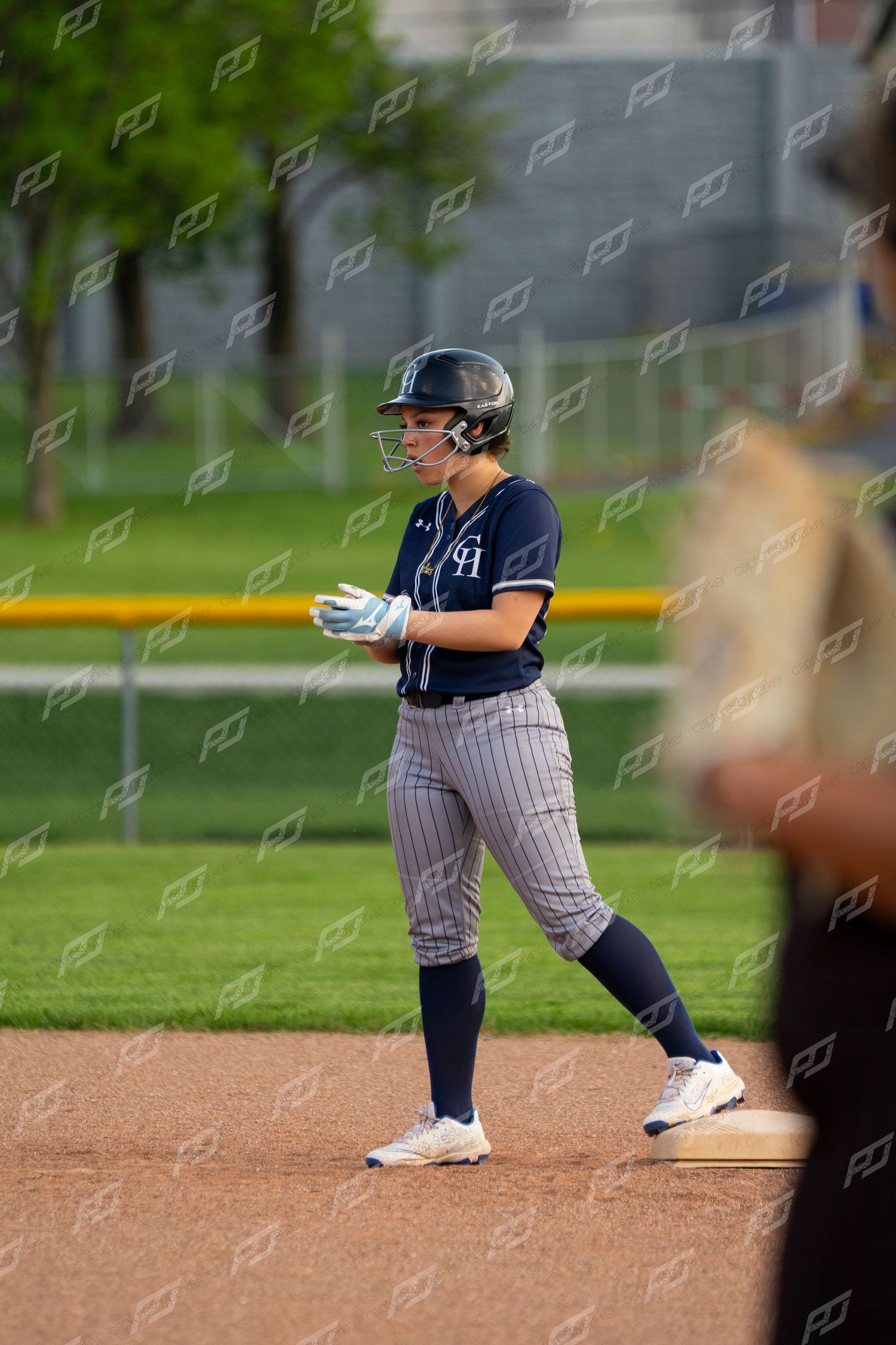 Female softball player in navy CH pinstripe uniform stands ready on base during outdoor game.