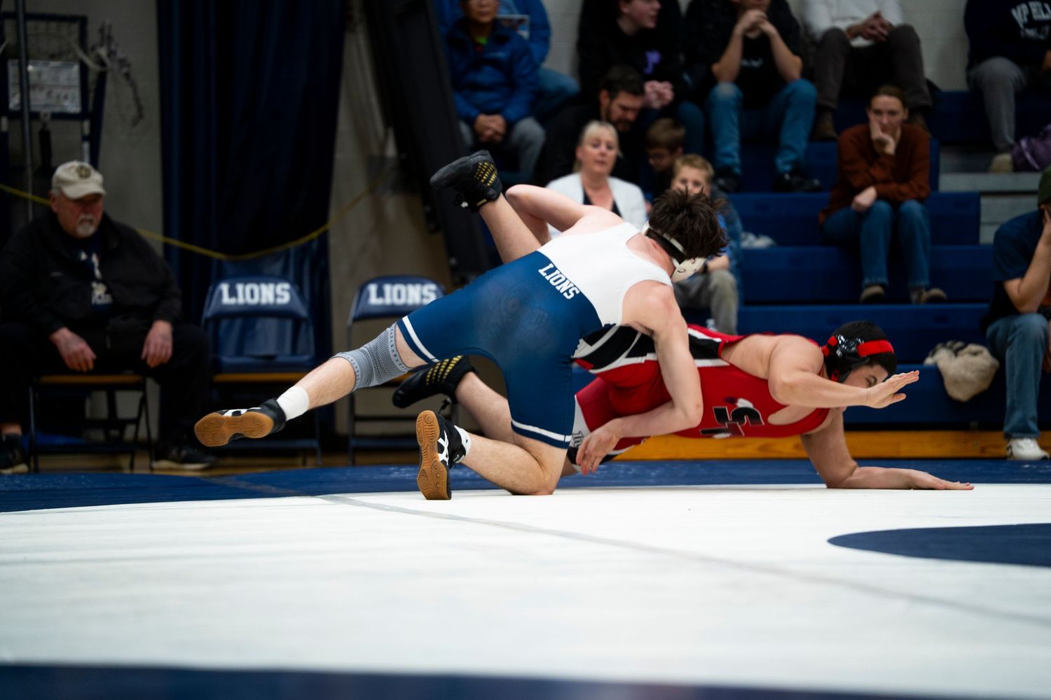 Two wrestlers in blue and red singlets grapple during an intense high school wrestling match.