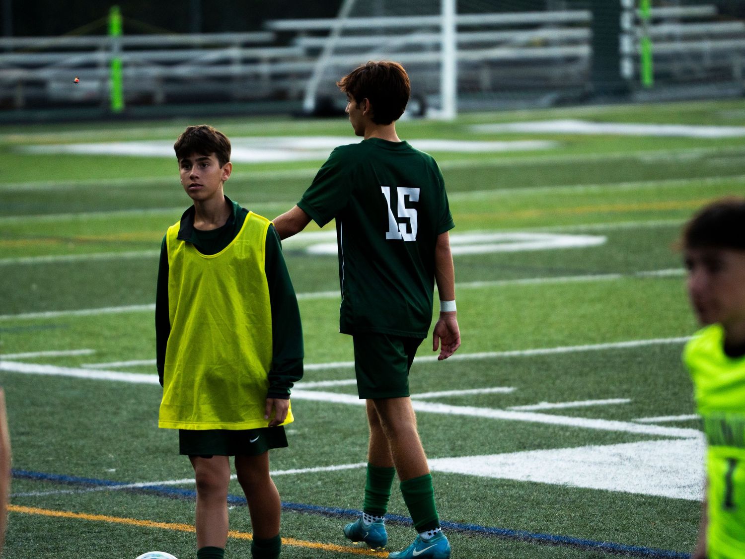 Two youth soccer players in green uniforms interact on the field during a soccer match.
