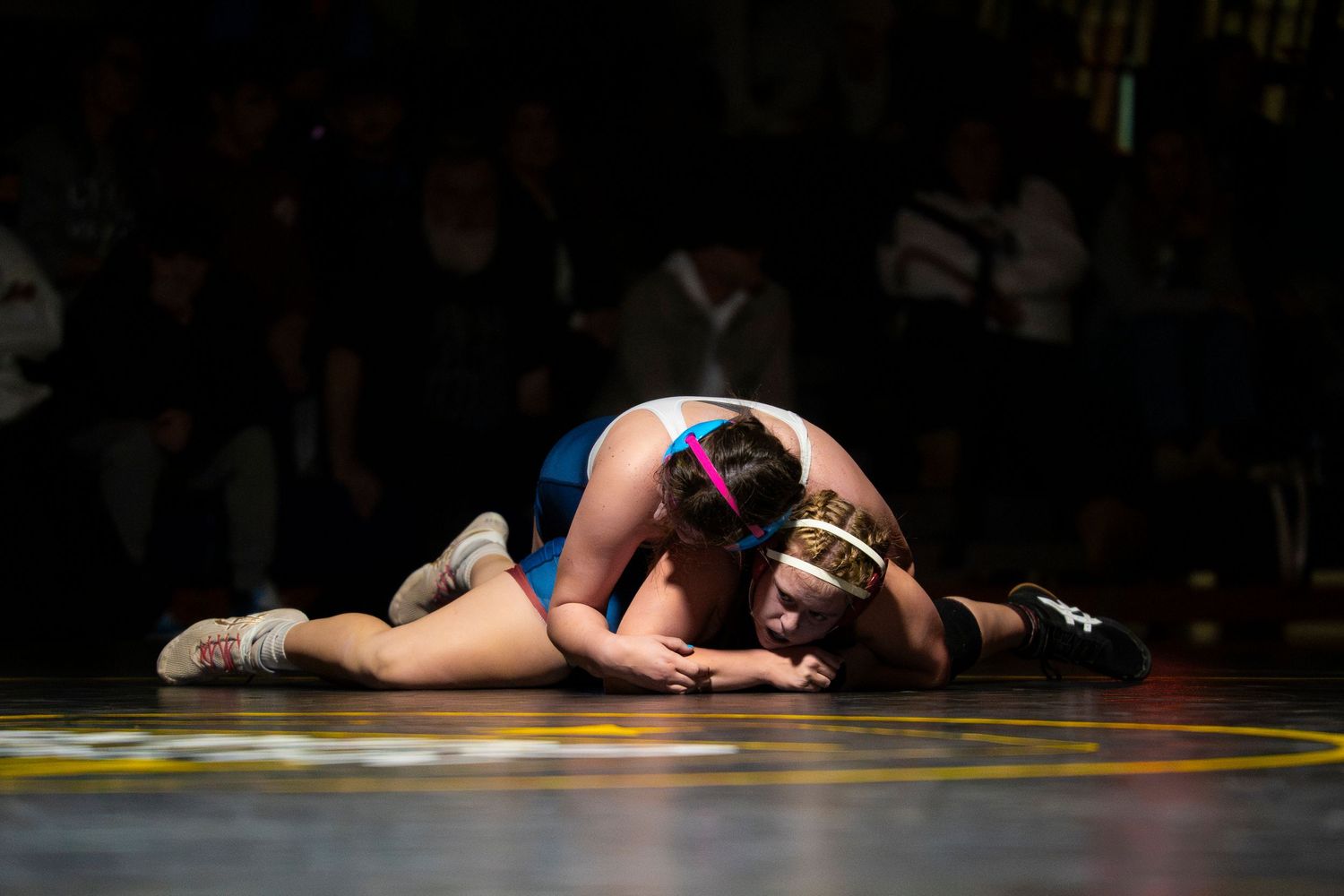 Female wrestler in blue singlet pins opponent during competitive indoor wrestling match.
