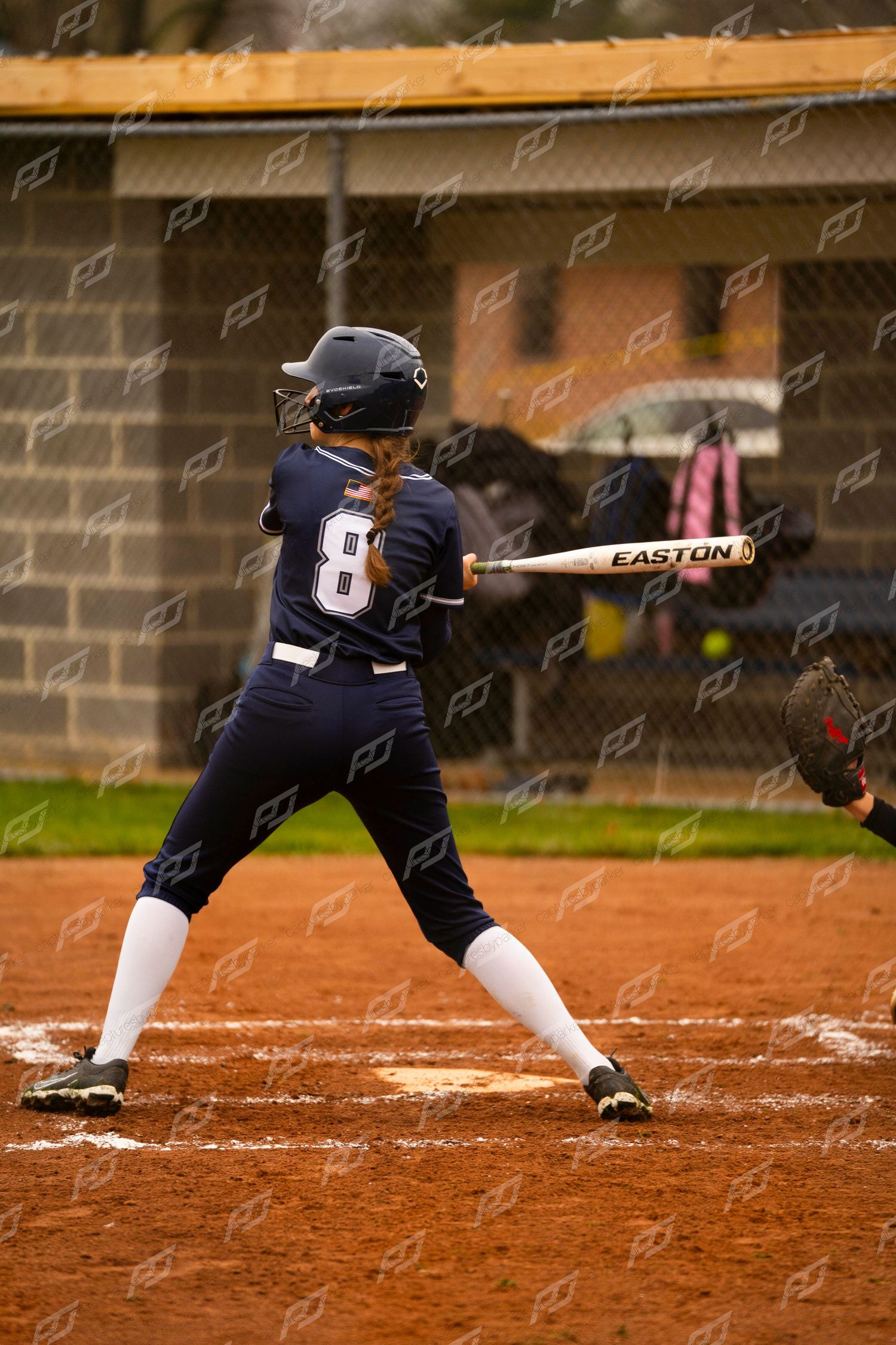 Female softball player #8 in navy uniform prepares to hit an incoming pitch with Easton bat.