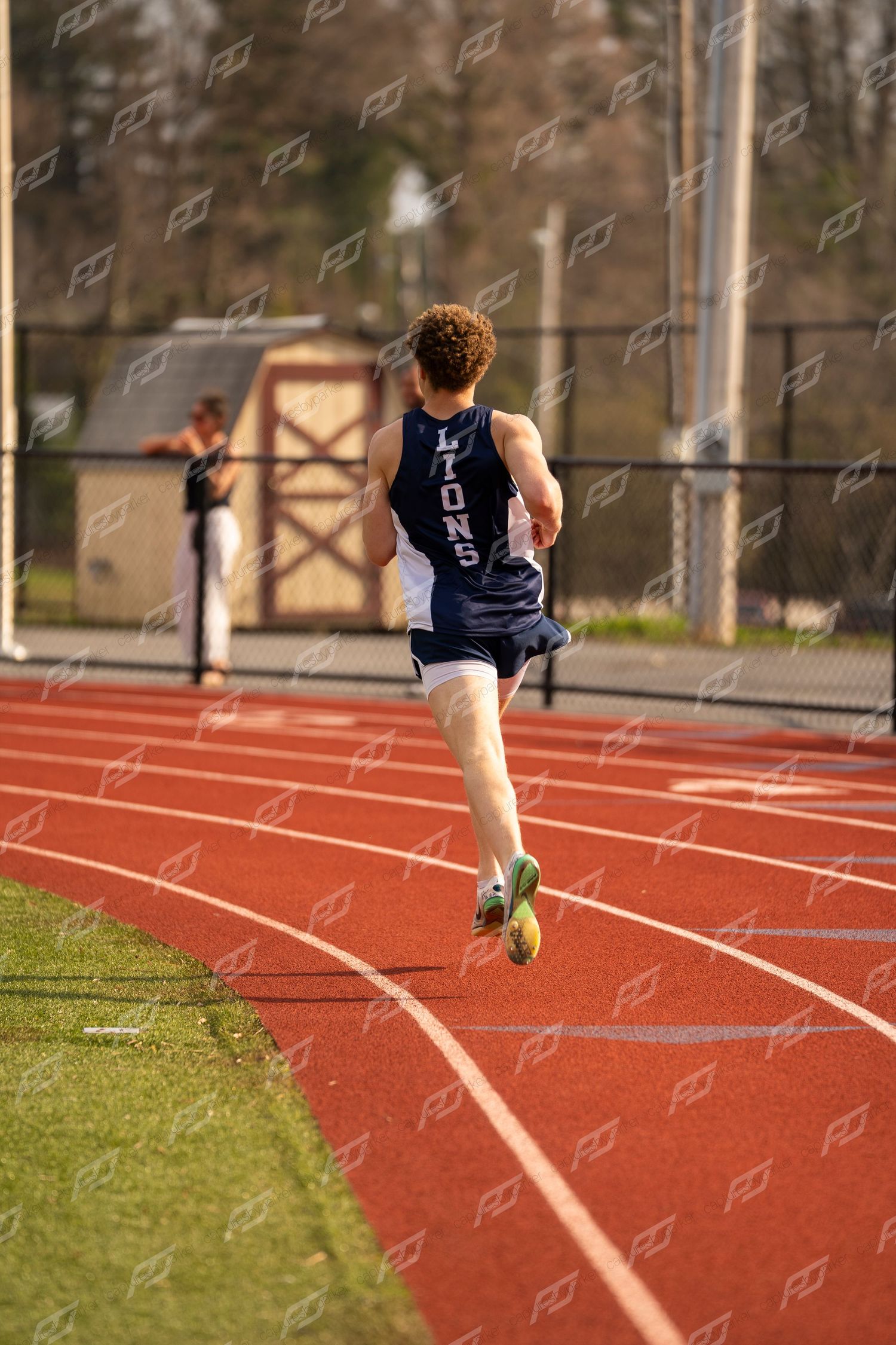 Male Lions track athlete running away from camera on red outdoor track.